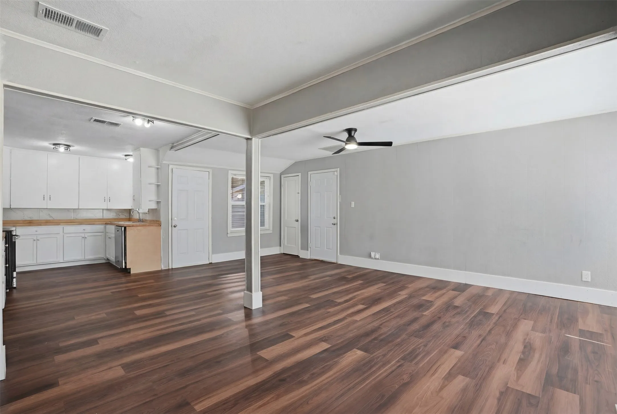 Spacious open-concept living area featuring wood-finish flooring, a ceiling fan, and white trim