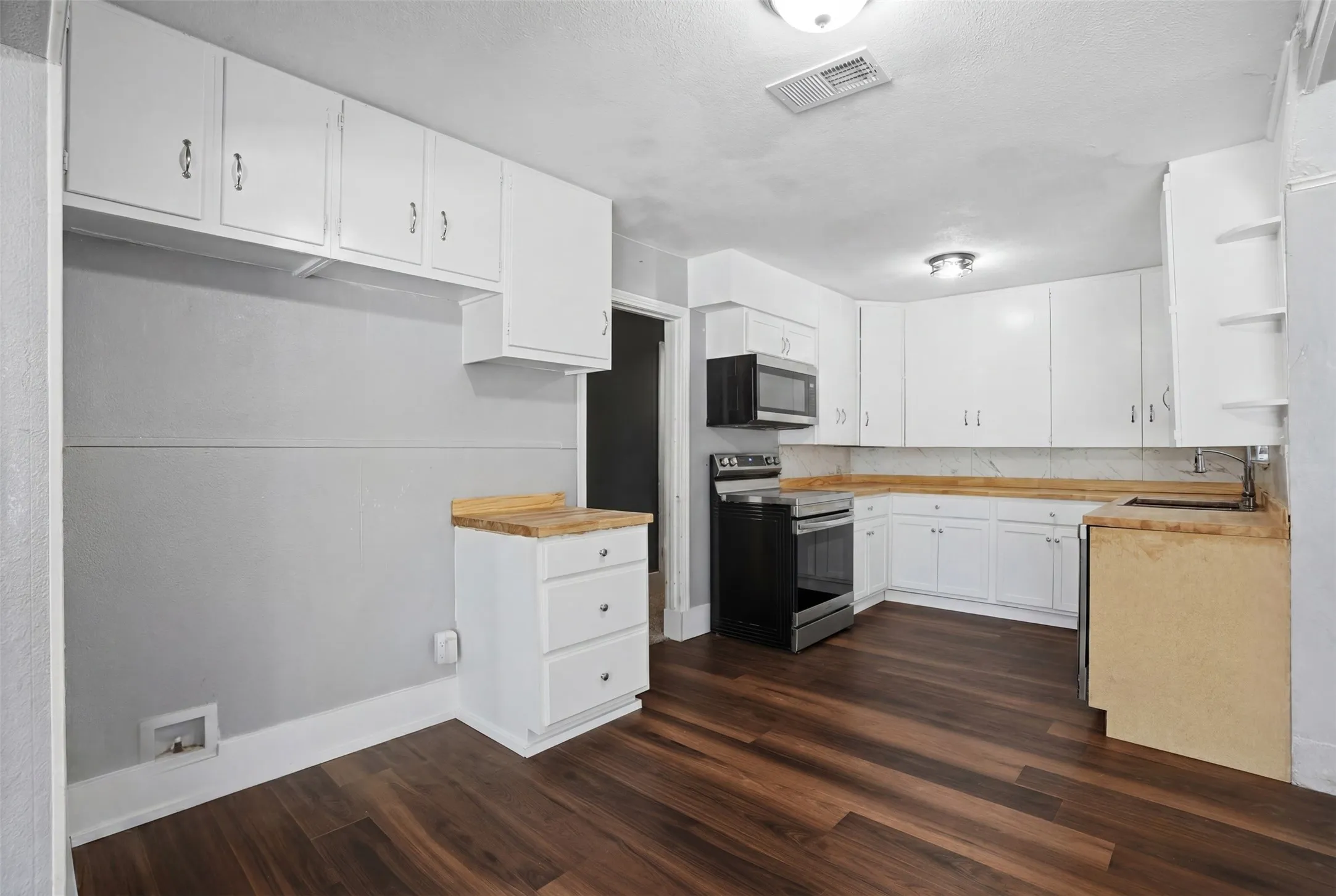 Kitchen featuring dark wood-finish flooring, white cabinetry, a stainless steel microwave, and a stainless steel electric range