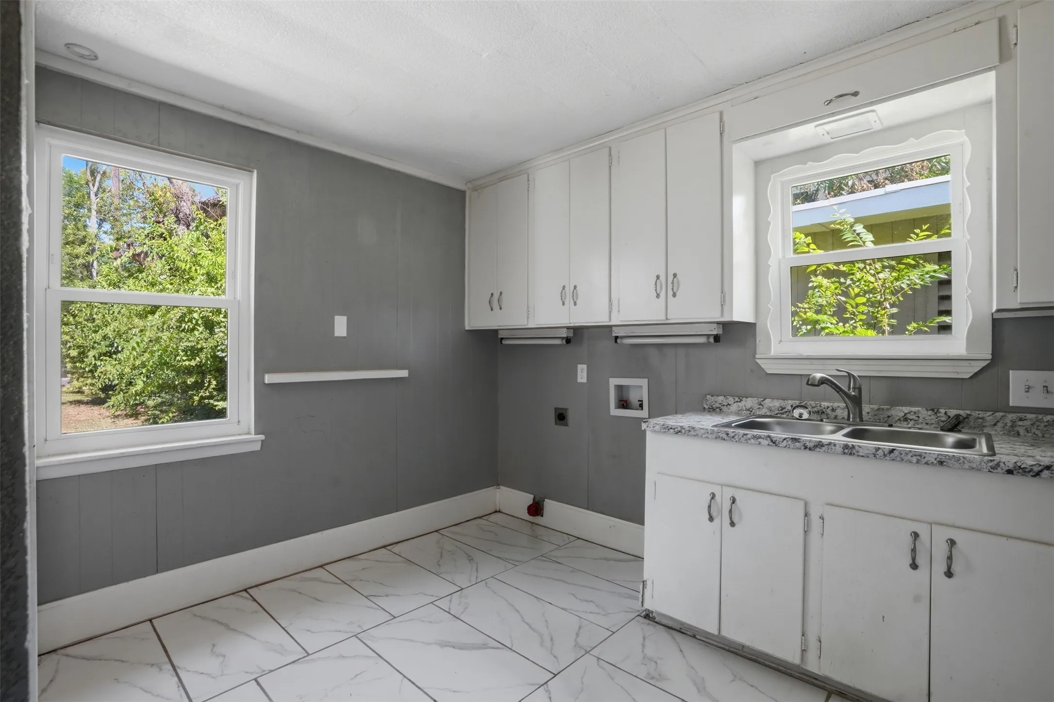 Utility area featuring expansive white-finish cabinetry, a dual-basin sink with a chrome faucet, speckled countertops, and large format tile flooring