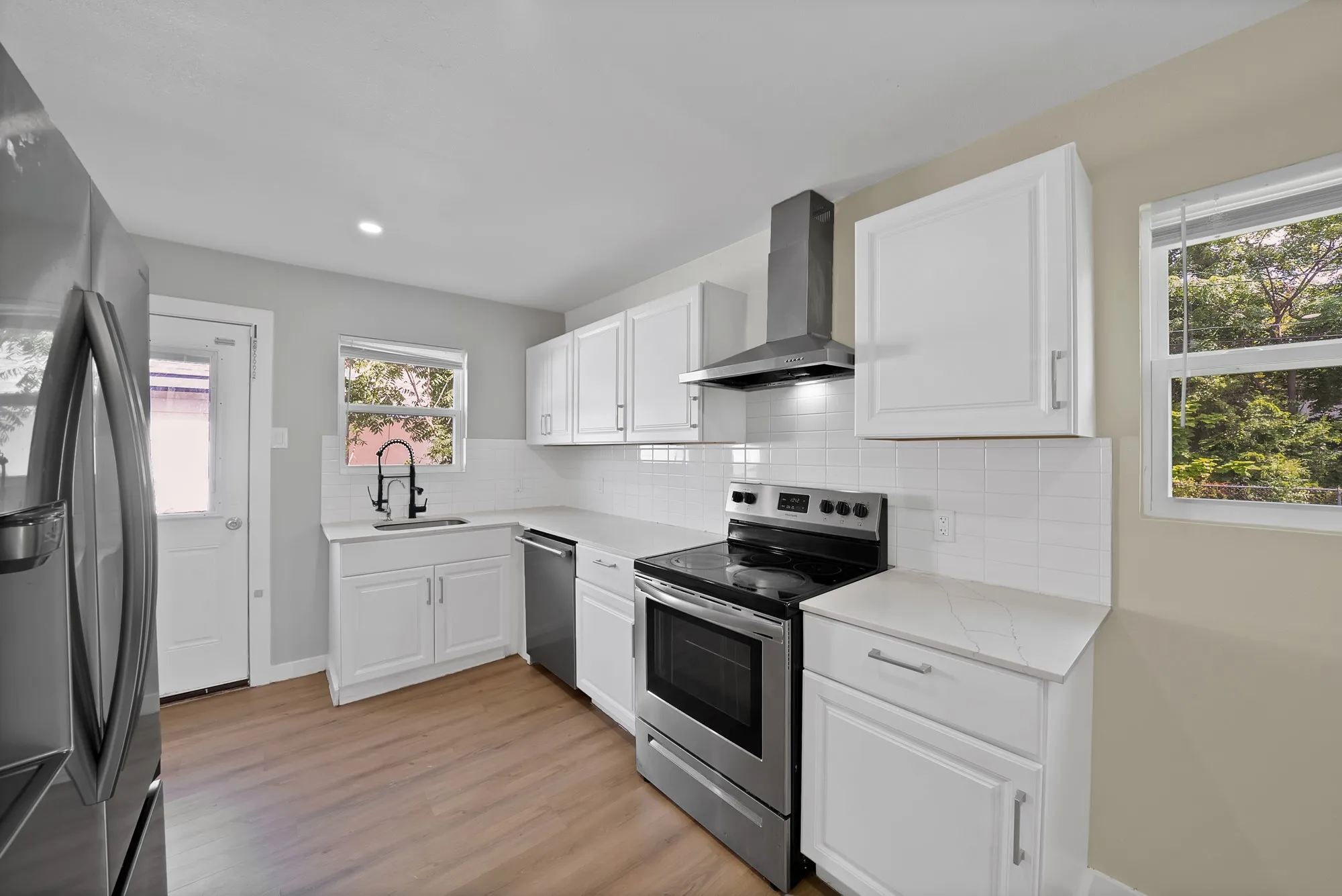 Modern kitchen featuring white shaker cabinetry, stainless steel appliances, white subway tile backsplash, light-toned countertops, and wood-finish flooring