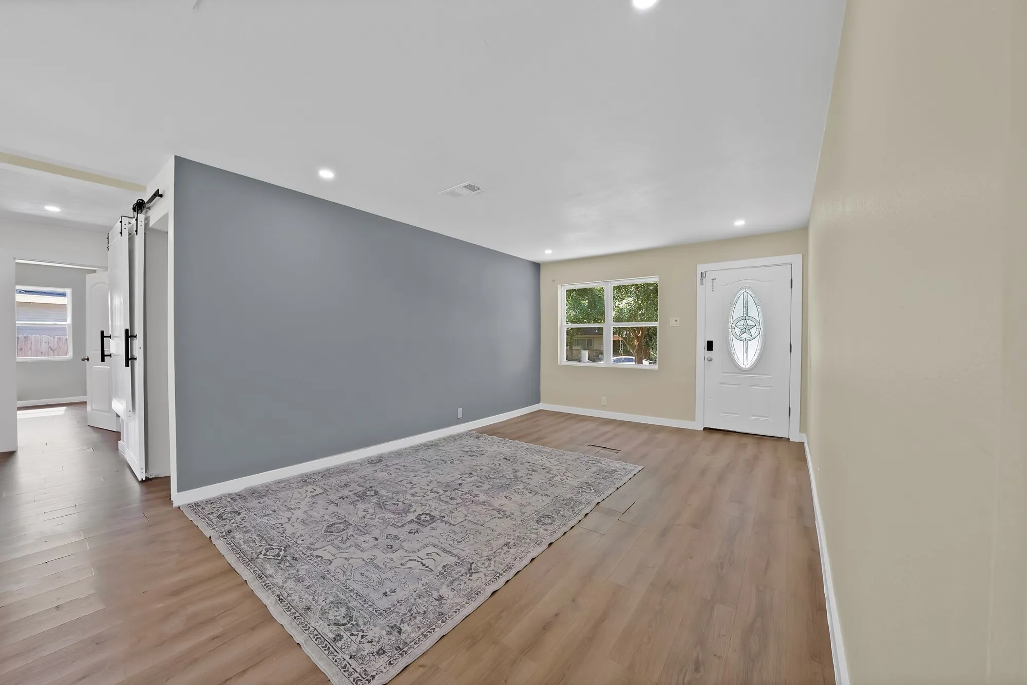 Open-concept living area featuring wood-finish flooring, recessed lighting, and a front entry door with an oval decorative glass insert