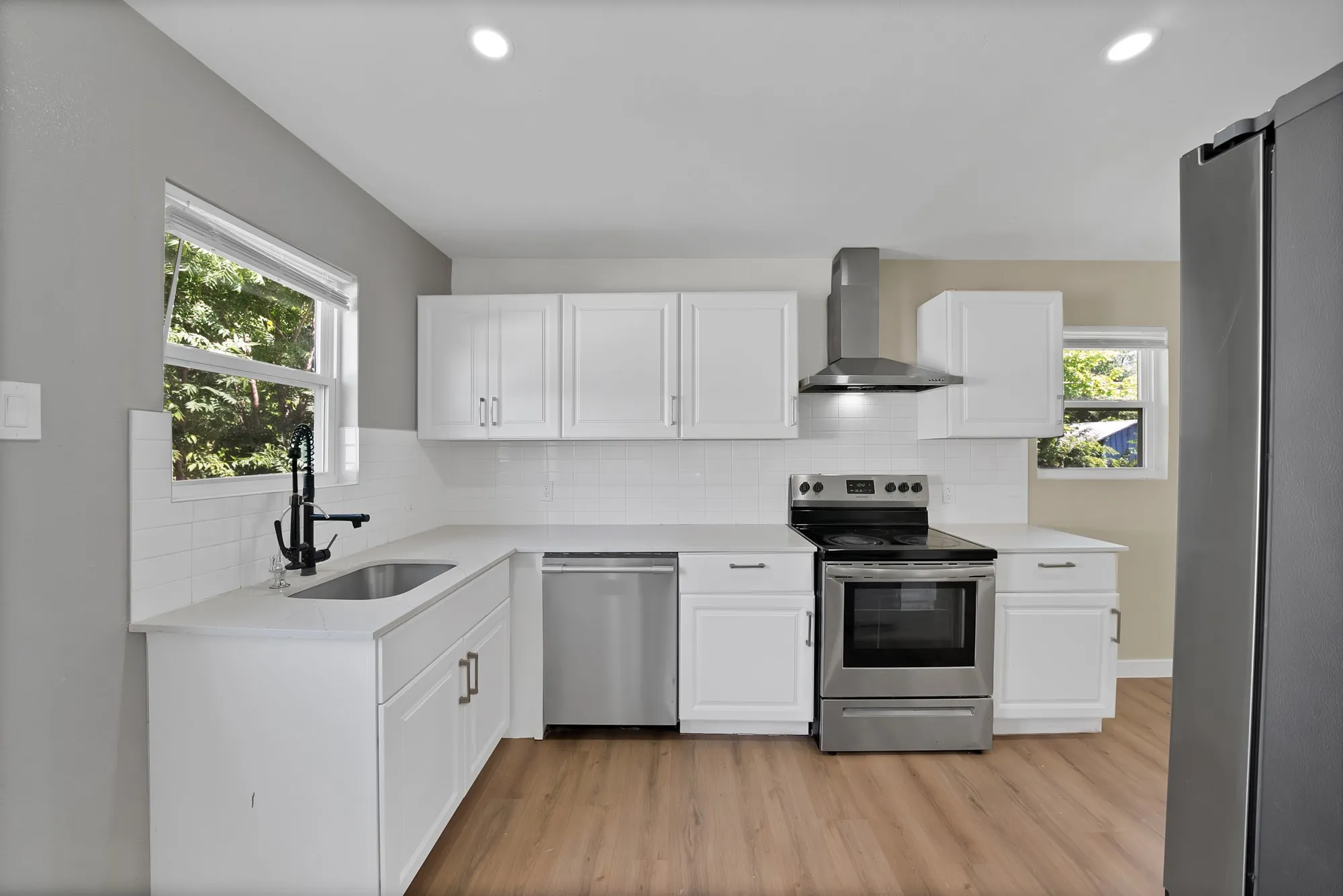 Contemporary kitchen featuring white cabinetry, light-toned countertops, stainless steel appliances, a subway tile backsplash, and wood-finish flooring