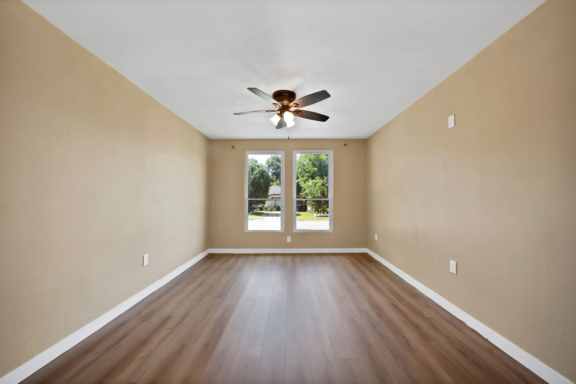 Spacious room featuring wood-finish flooring, neutral-toned walls, and white baseboards