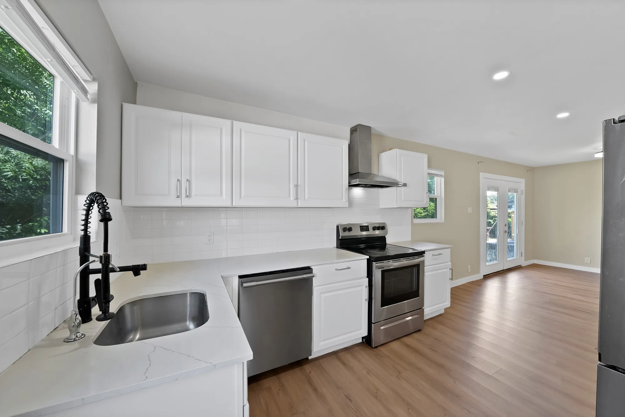 Kitchen featuring white cabinetry, light-toned countertops, stainless steel appliances, and wood-finish flooring