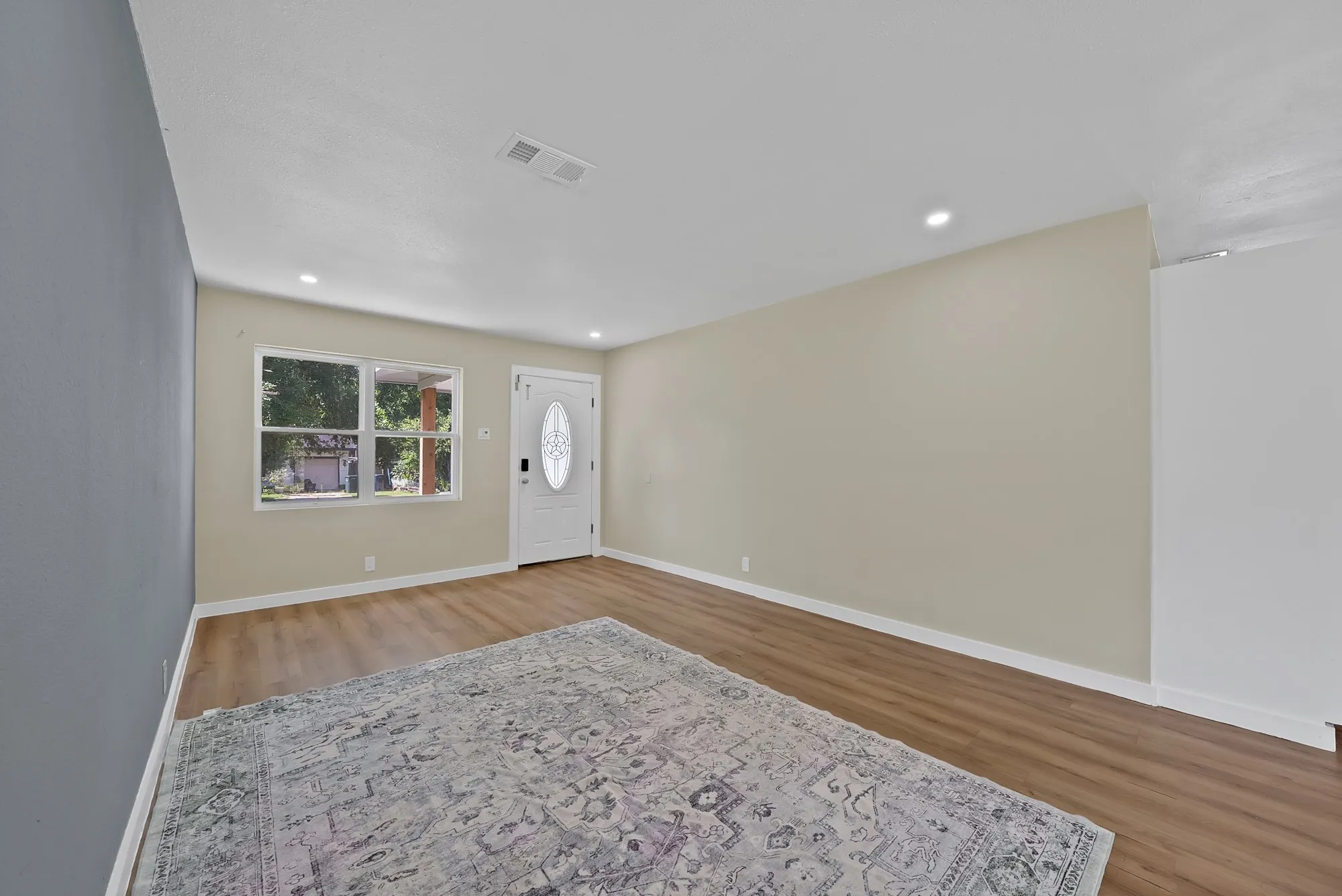 Spacious room featuring wood-finish flooring, recessed lighting, and a front entry door with an oval-shaped decorative glass insert