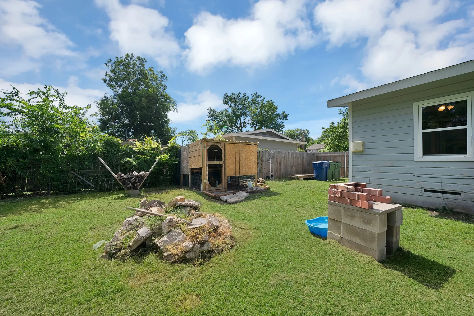 Expansive backyard with a manicured lawn, established perimeter landscaping, and a built-in outdoor cooking structure constructed from concrete blocks and bricks
