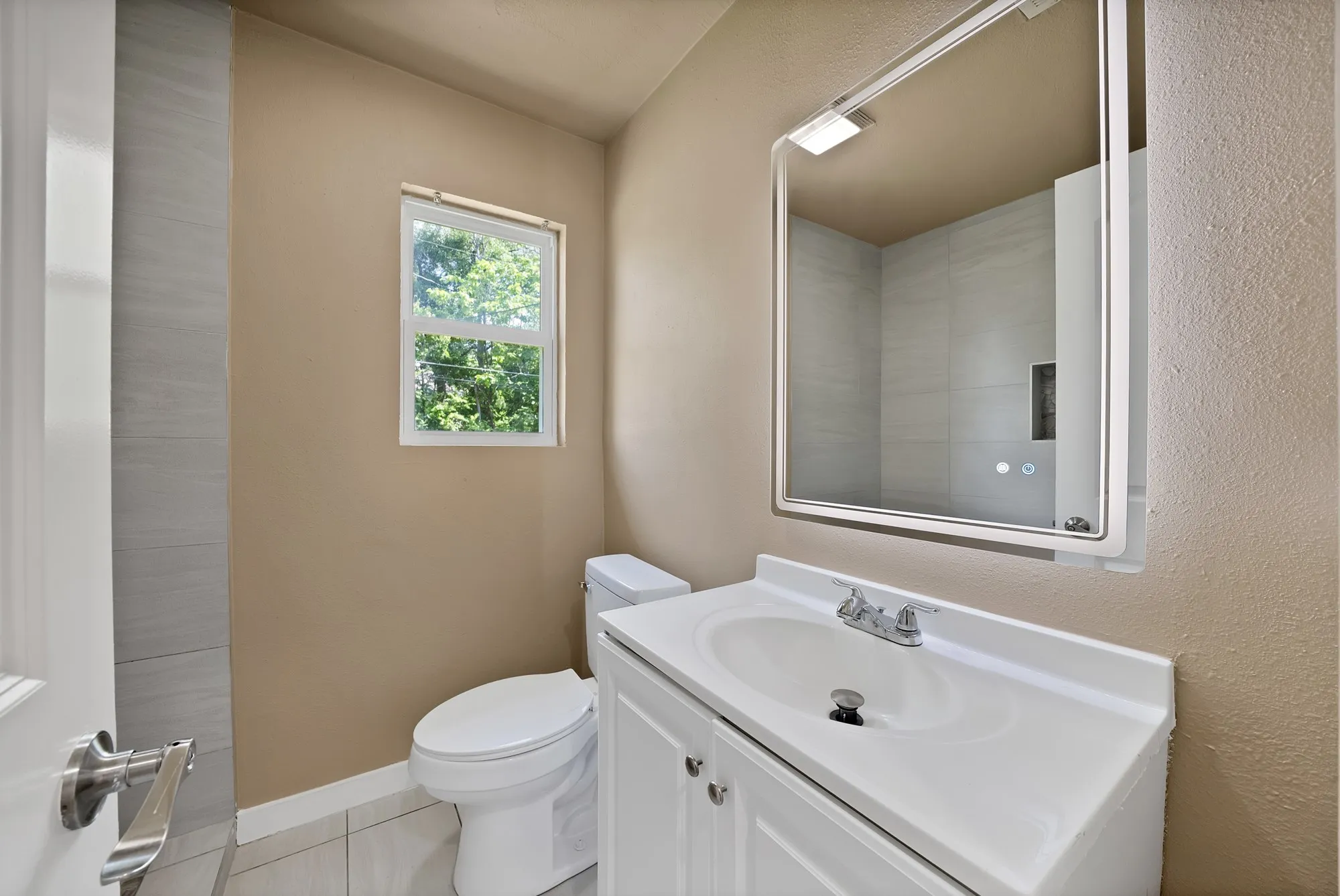 Bathroom featuring a white vanity with integrated sink, chrome faucet, and a lighted mirror