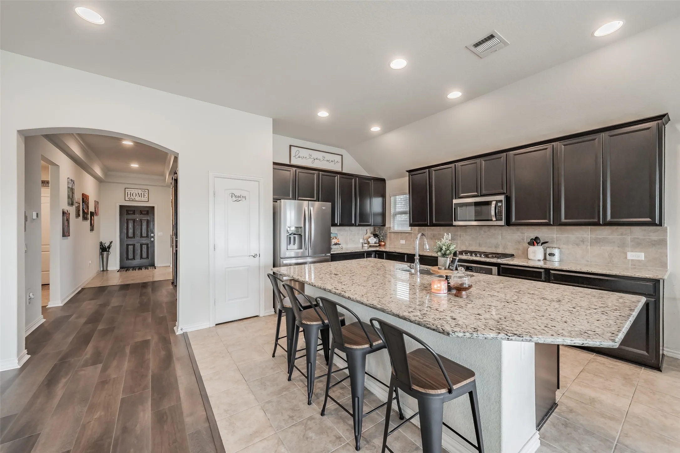 Expansive kitchen island with a granite countertop, dark cabinetry, and stainless steel appliances