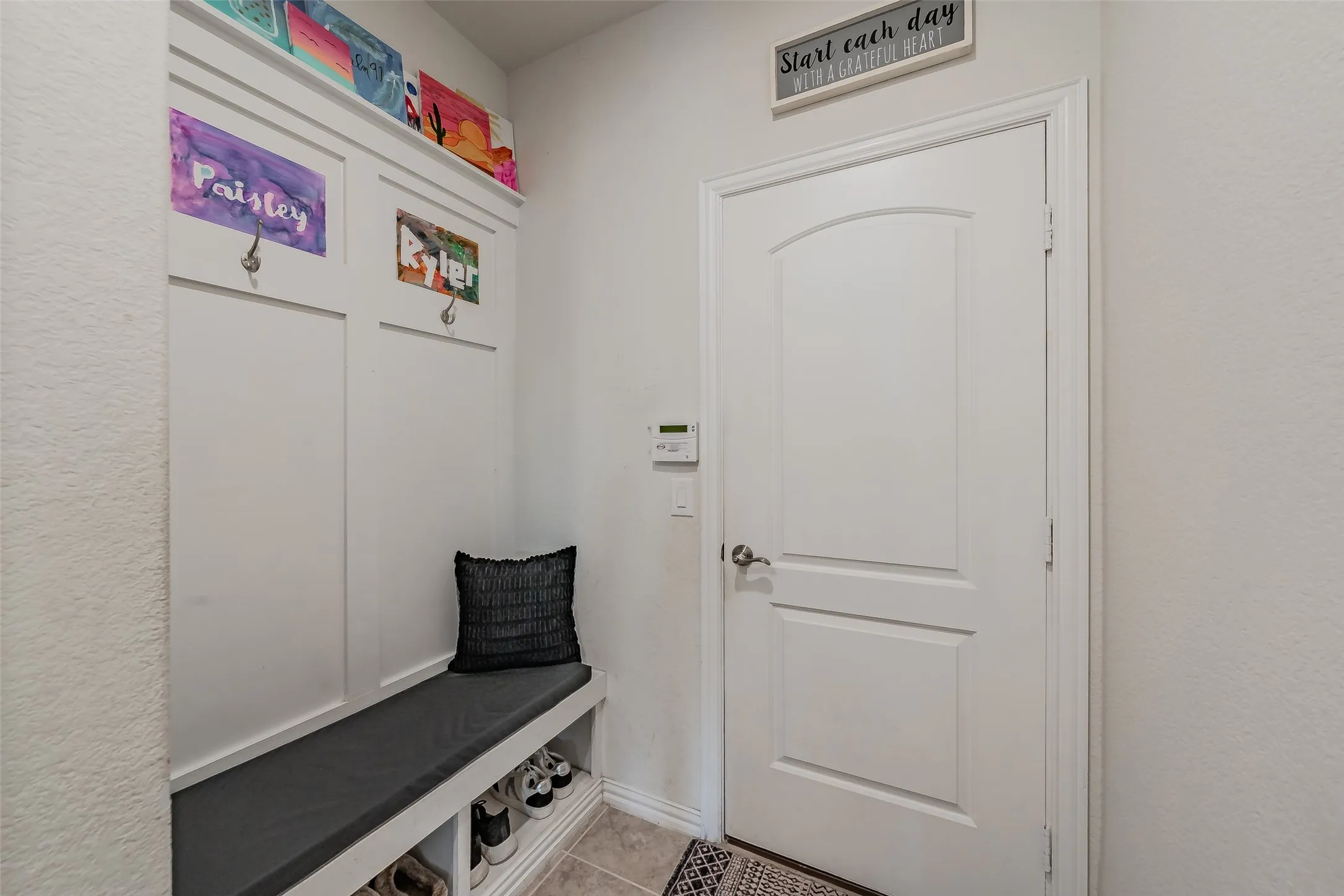 Convient mud room with built-in cushioned bench with hooks, located just inside garage door entrance