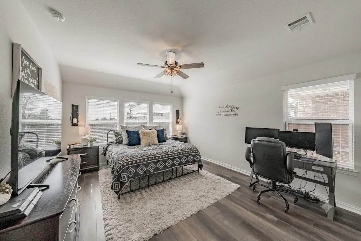 Spacious primary bedroom featuring laminate wood-finish flooring, a vaulted ceiling, and multiple windows for natural lighting