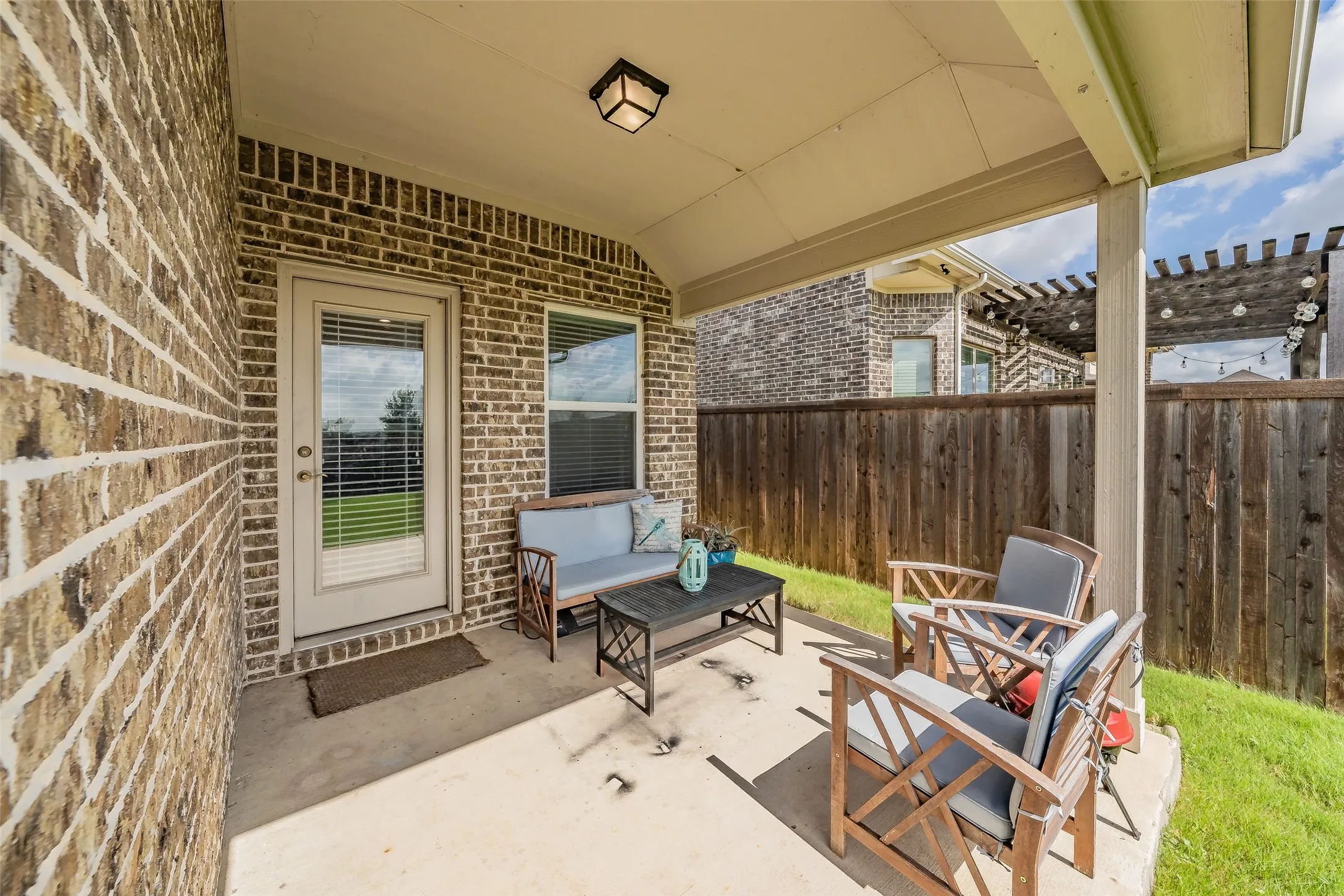Covered back patio featuring a brick exterior wall and a privacy fence