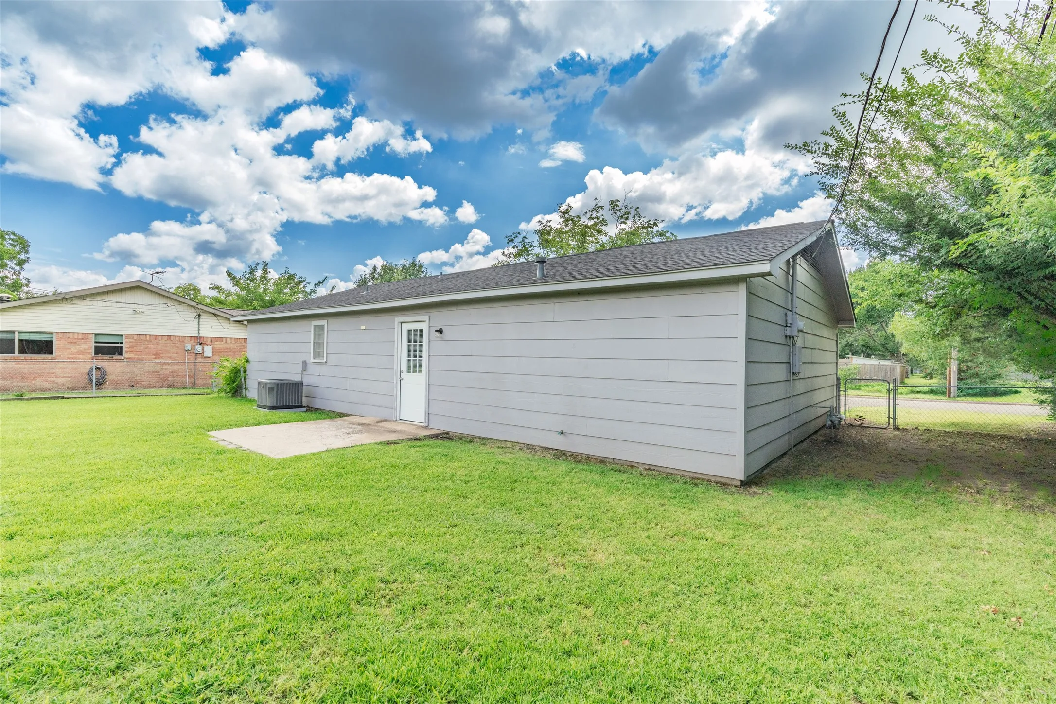 Expansive green lawn with a detached building featuring horizontal siding and a side entry door