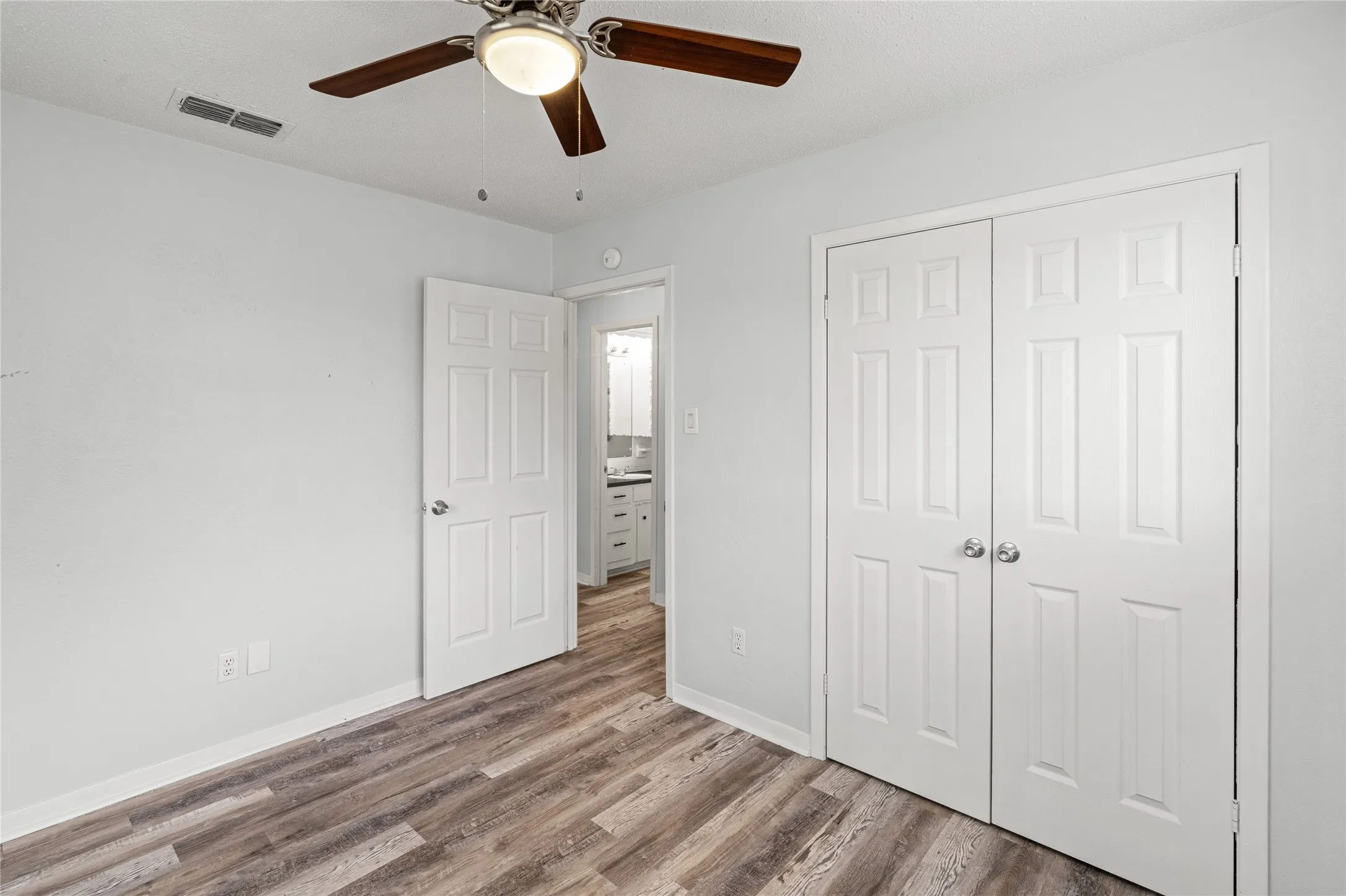 Room featuring wood-finish flooring, a ceiling fan with integrated lighting, and white walls