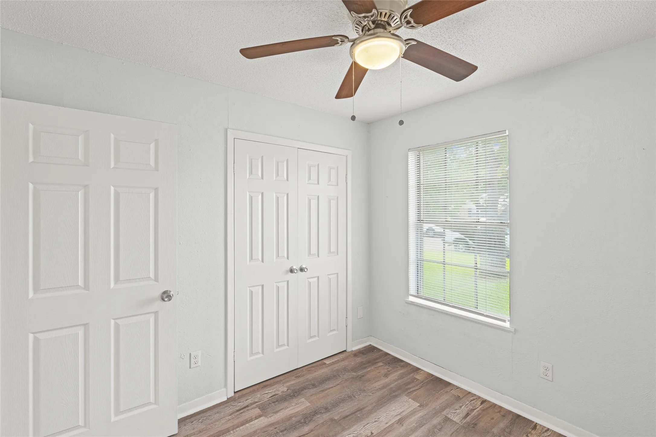 Interior space featuring wood-finish flooring, a white window with blinds, and a ceiling fan with integrated lighting
