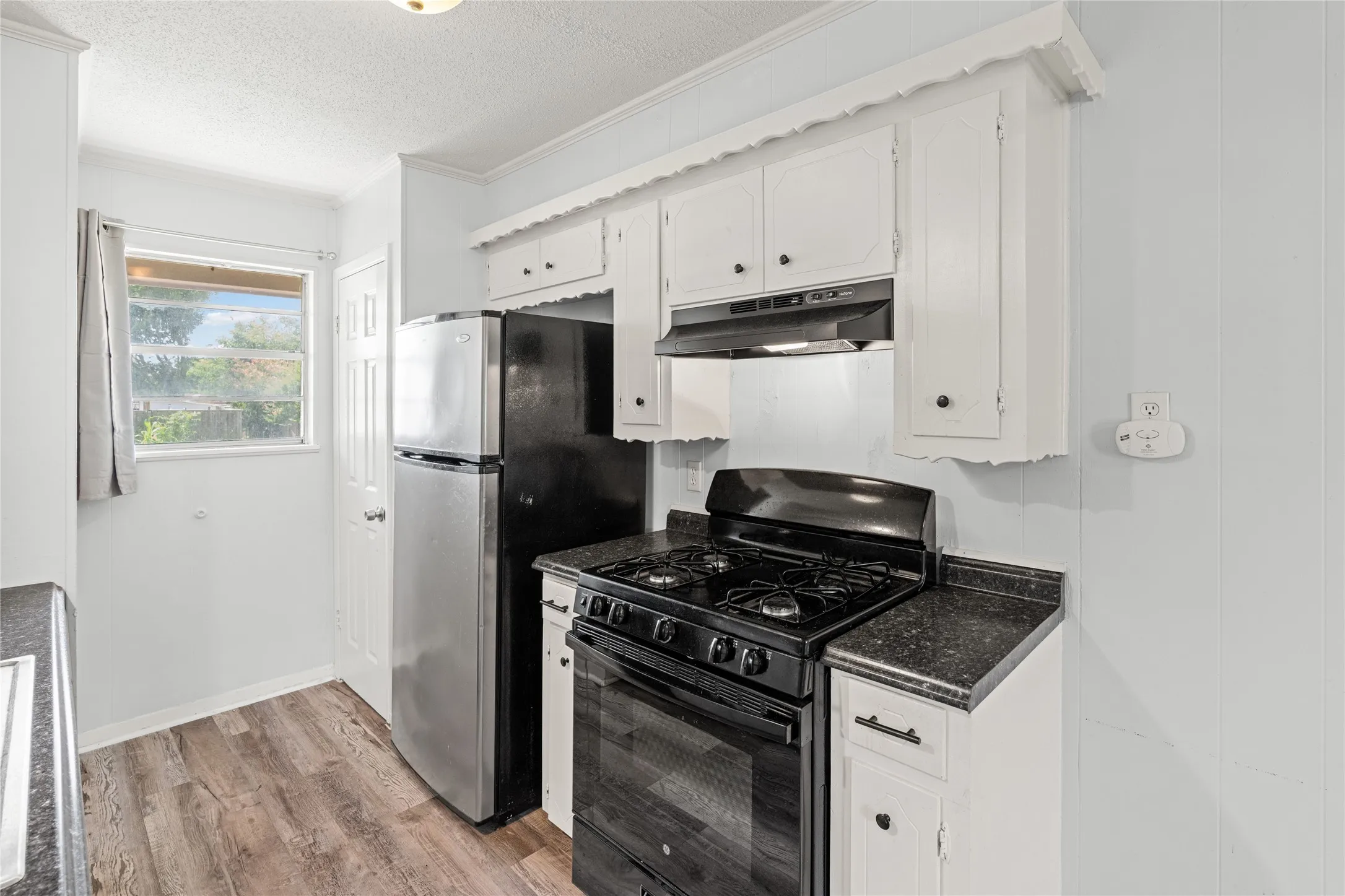 Kitchen featuring white cabinetry, black countertops, a stainless steel refrigerator, a black gas range, and wood-finish flooring