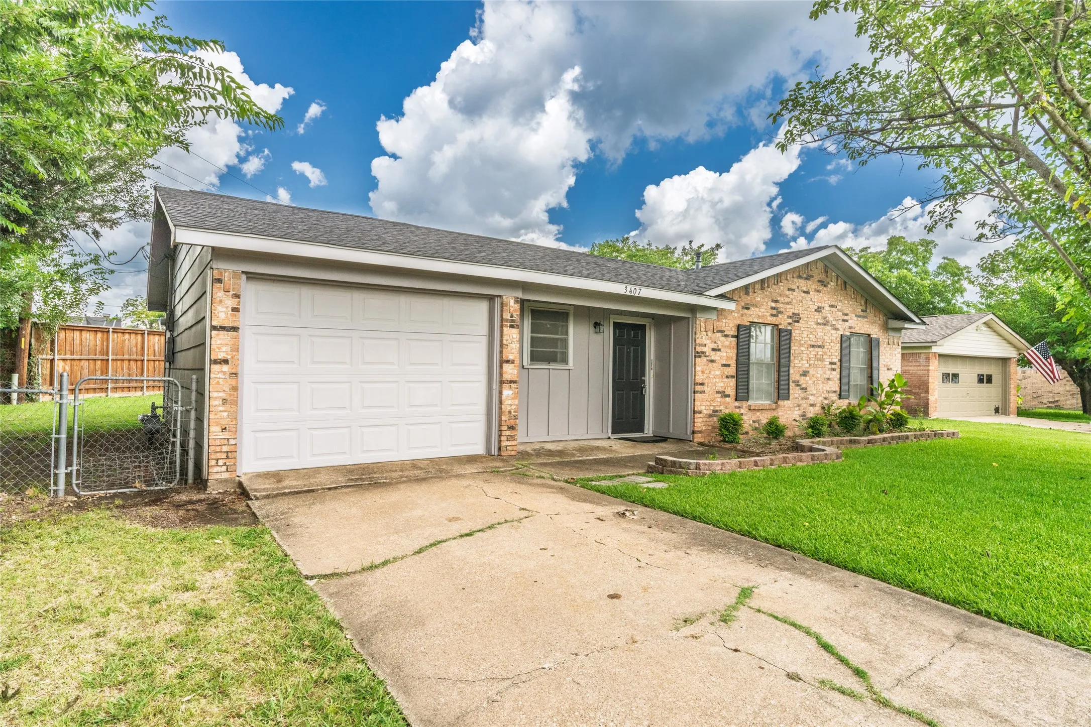 Brick and siding exterior with an attached garage, a paved driveway, and a chain-link fence