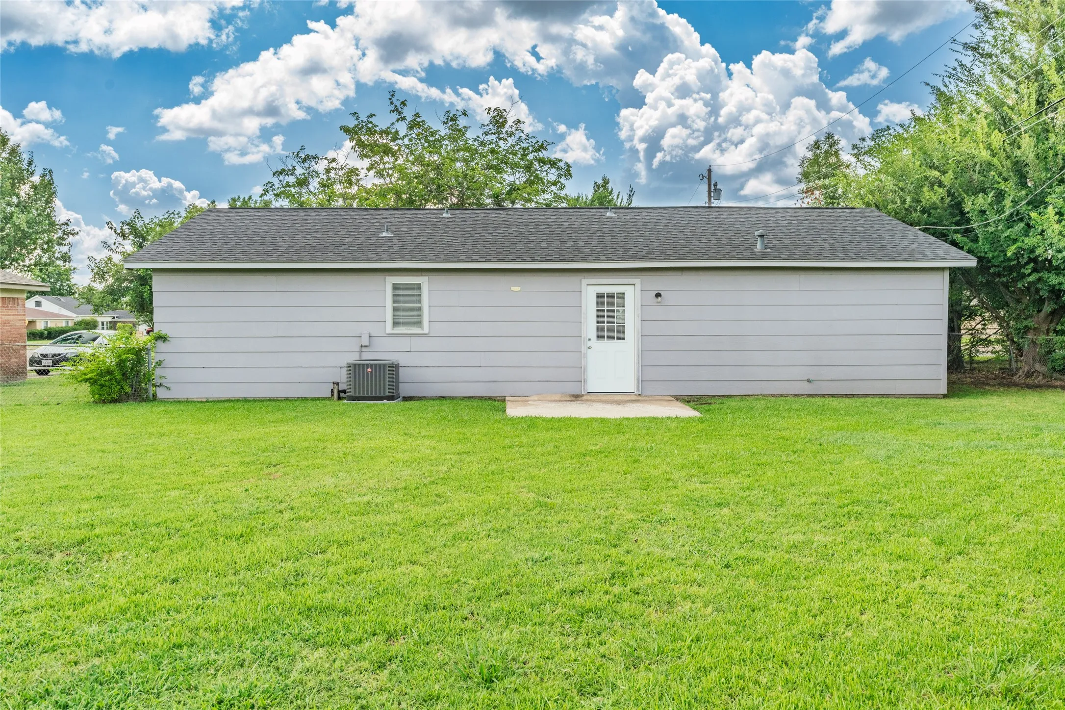 Expansive green lawn with a gray exterior, white entry door, and a single-pane window