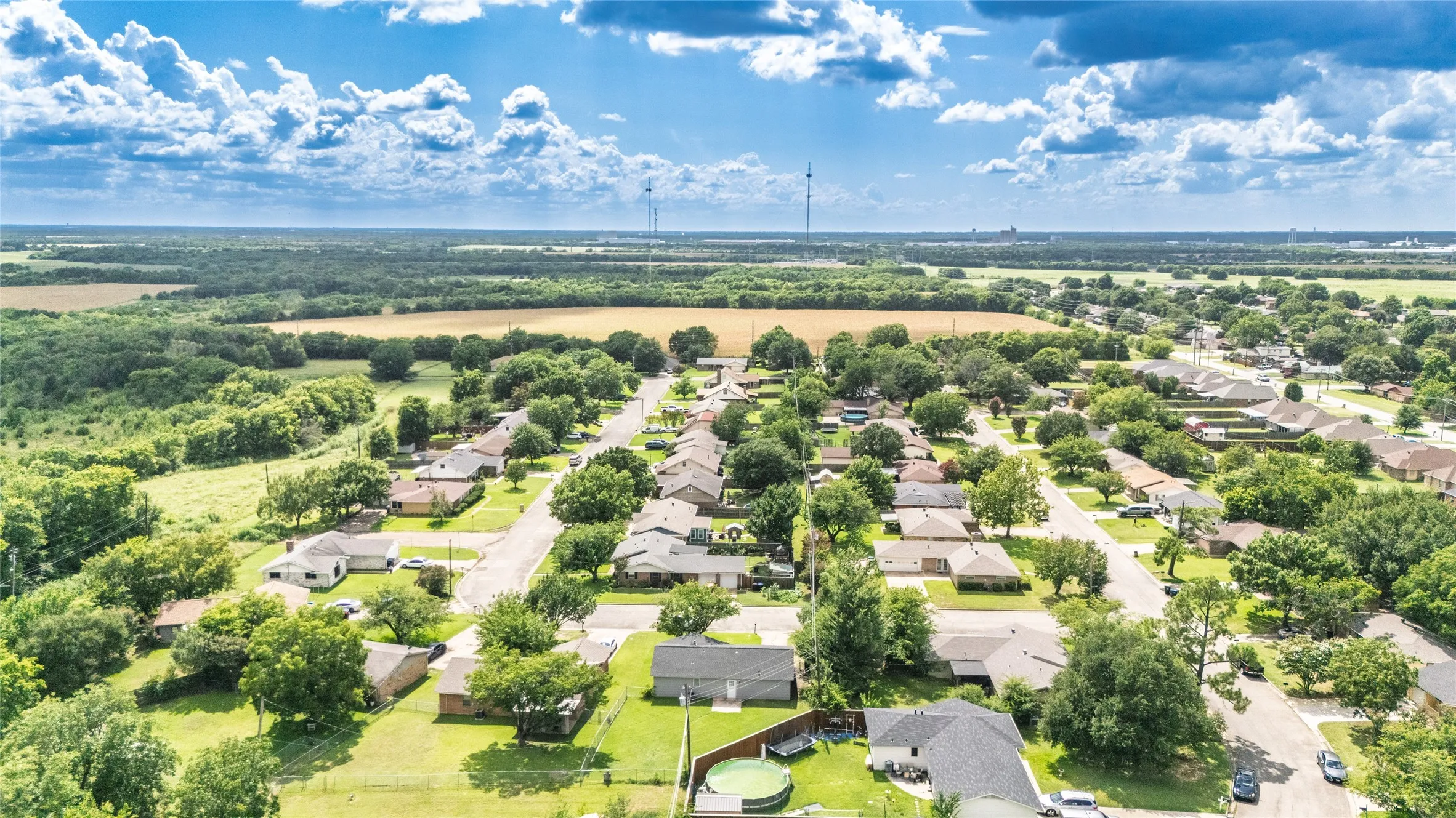 Residential neighborhood featuring single-story homes with dark shingle roofs, mature trees, paved streets, and expansive green spaces