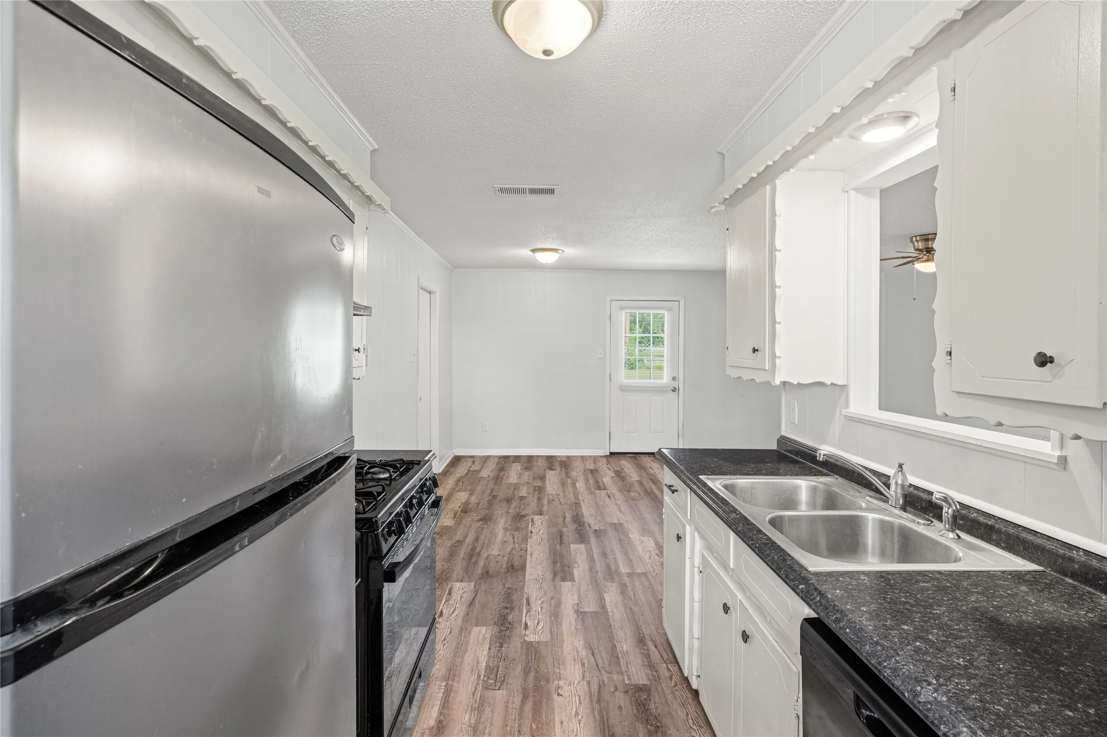 Kitchen featuring a stainless steel refrigerator, black gas range, dual basin stainless steel sink, black countertops, and white cabinetry