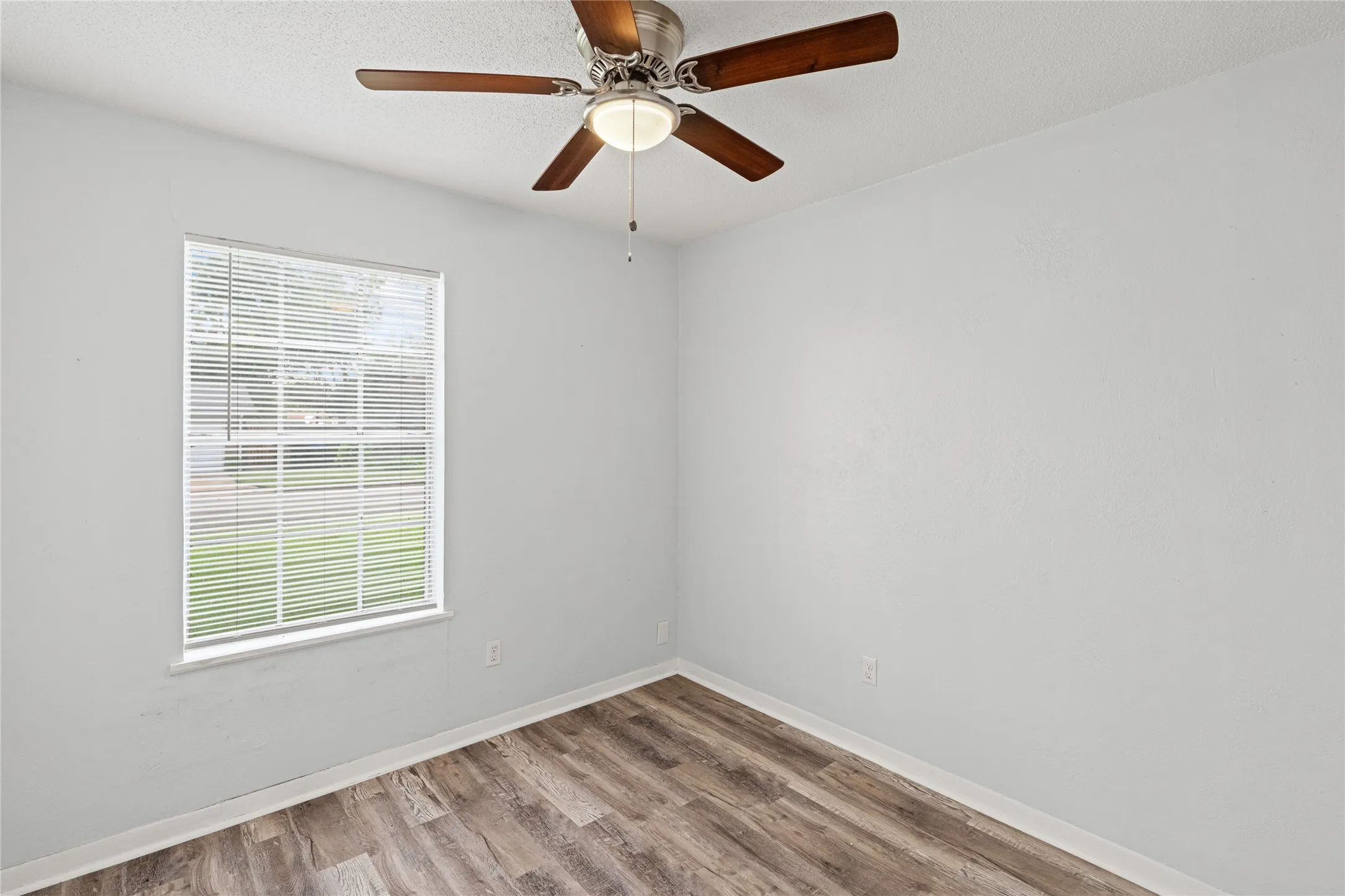 Room featuring wood-finish flooring, a ceiling fan with integrated lighting, and a window with blinds