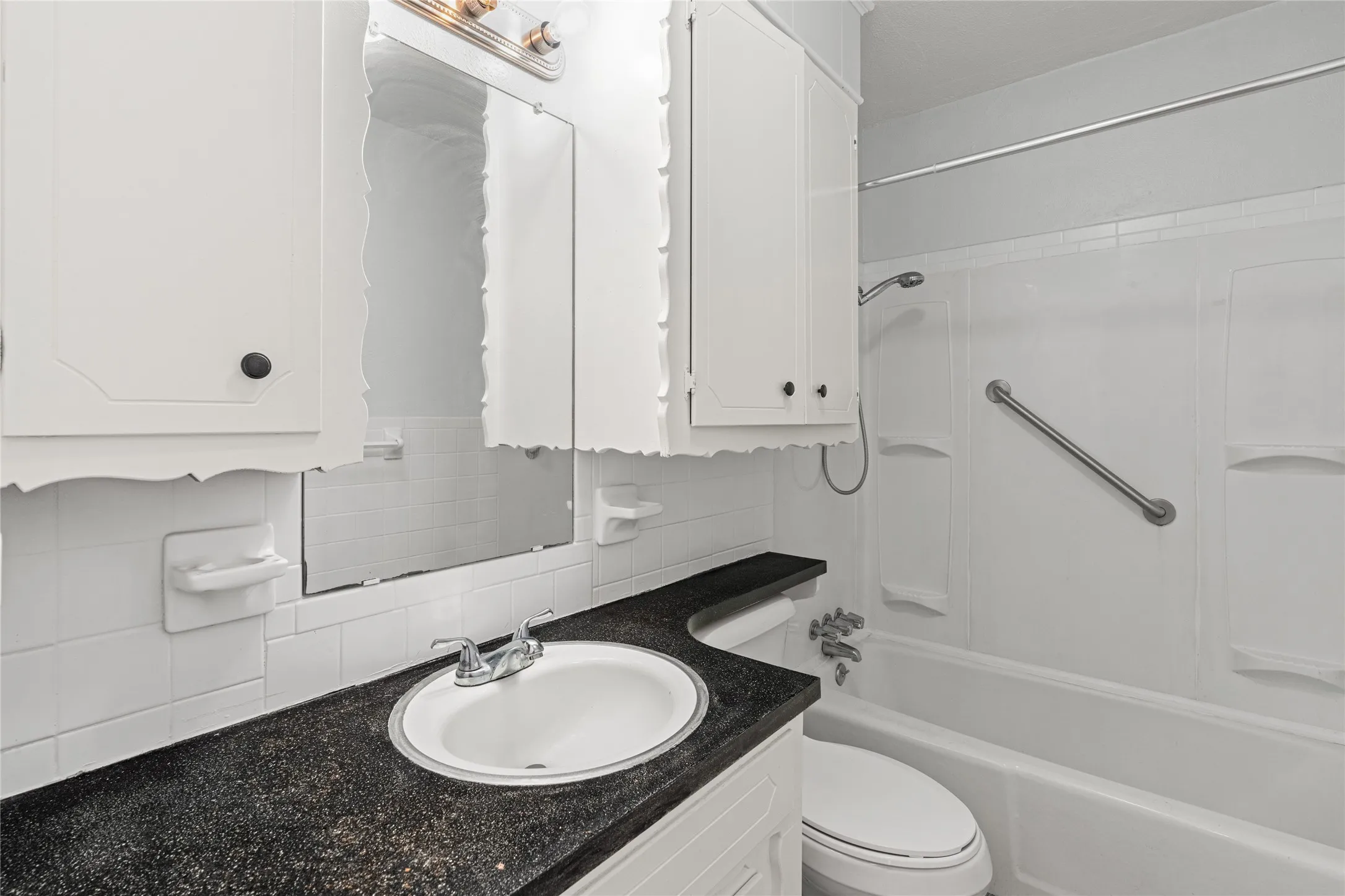 White bathroom featuring a built-in tub with a shower head, grab bar, and wall-mounted shower caddy