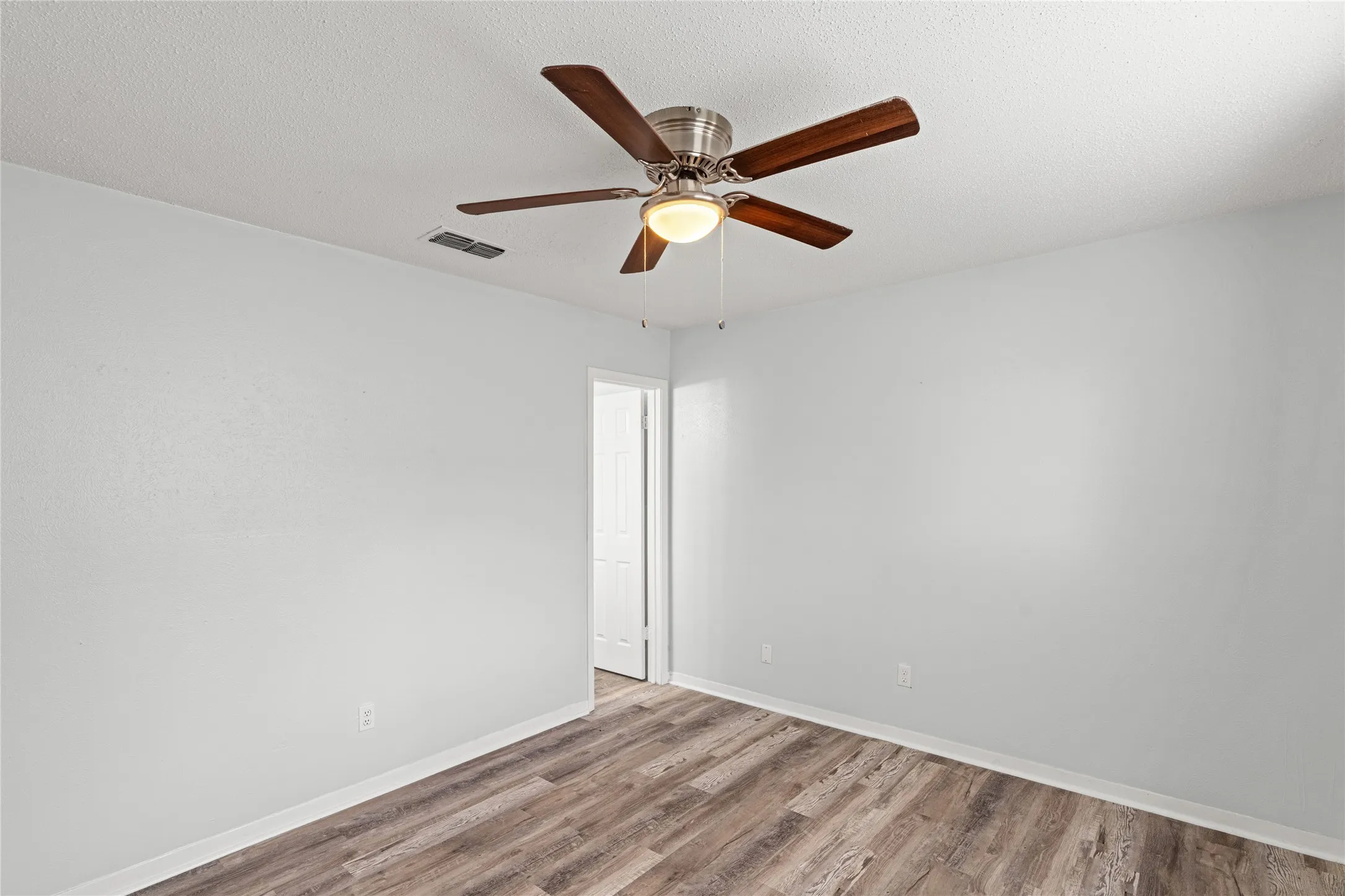 Room featuring wood-finish flooring, light grey walls, white baseboards, and a ceiling fan with integrated lighting
