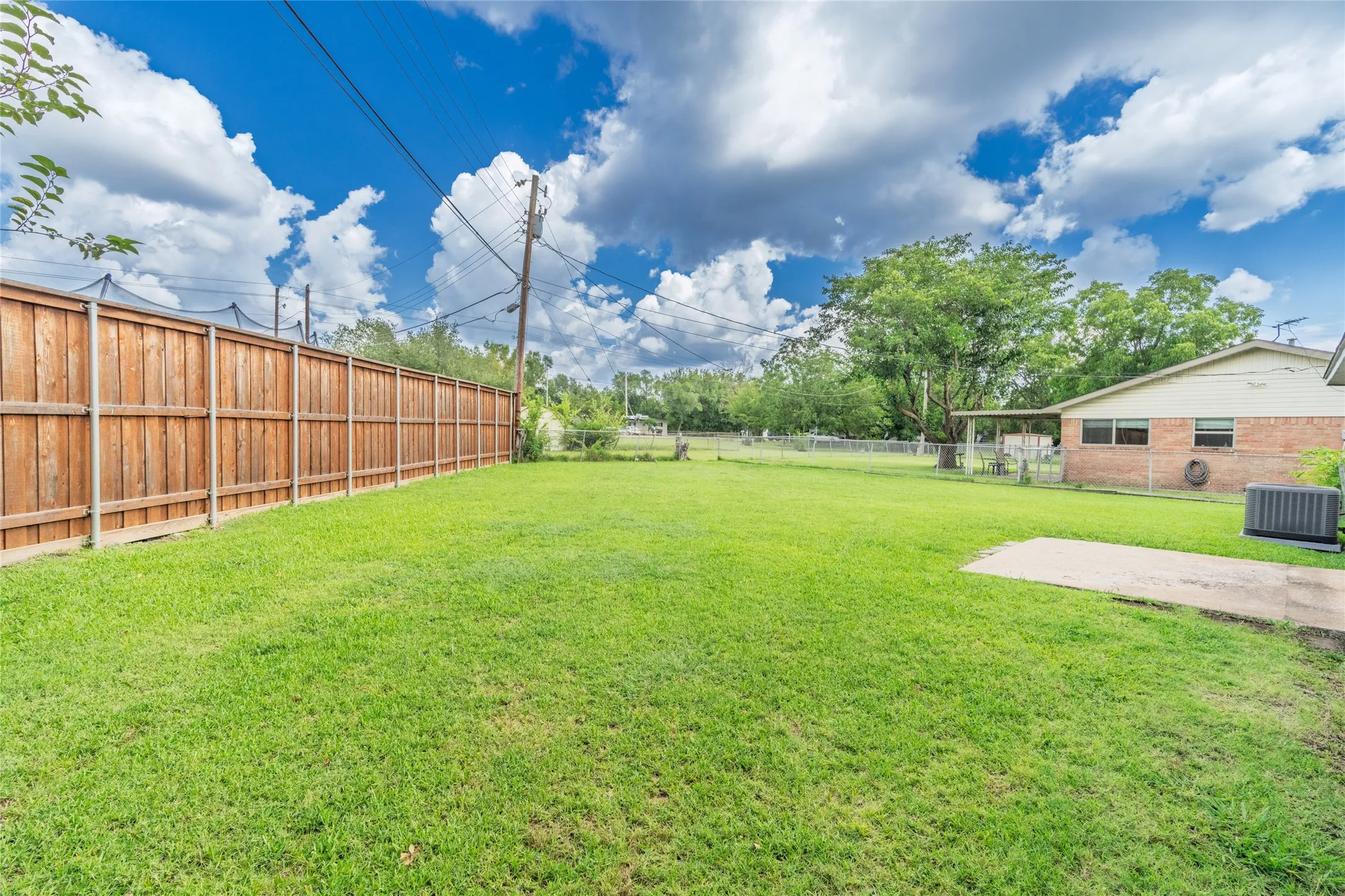 Expansive backyard featuring a manicured lawn, full wood privacy fencing, and a concrete patio pad