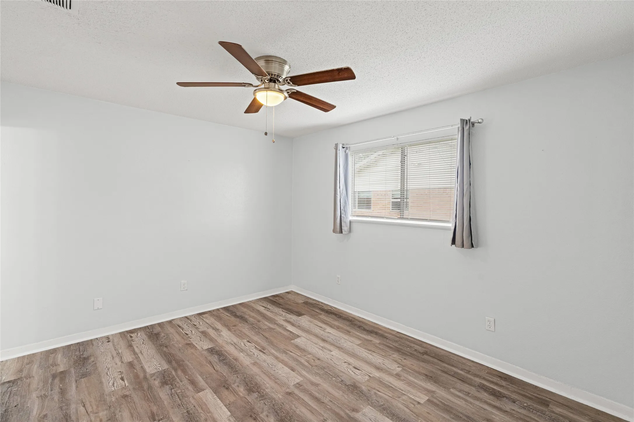 Spacious room featuring wood-finish flooring and a ceiling fan with integrated lighting