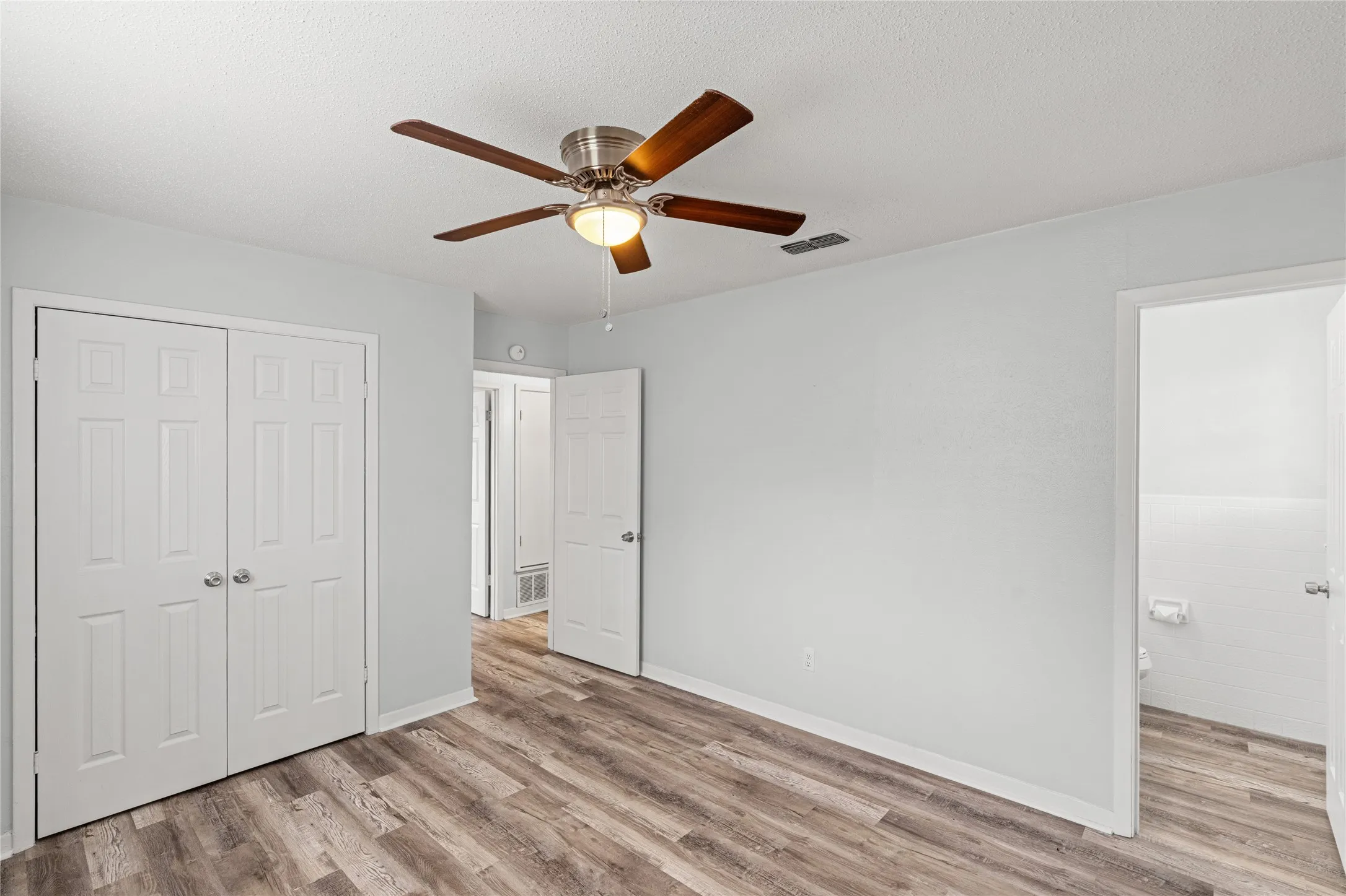 Spacious room featuring wood-finish flooring, a ceiling fan with light fixture, and white bi-fold closet doors