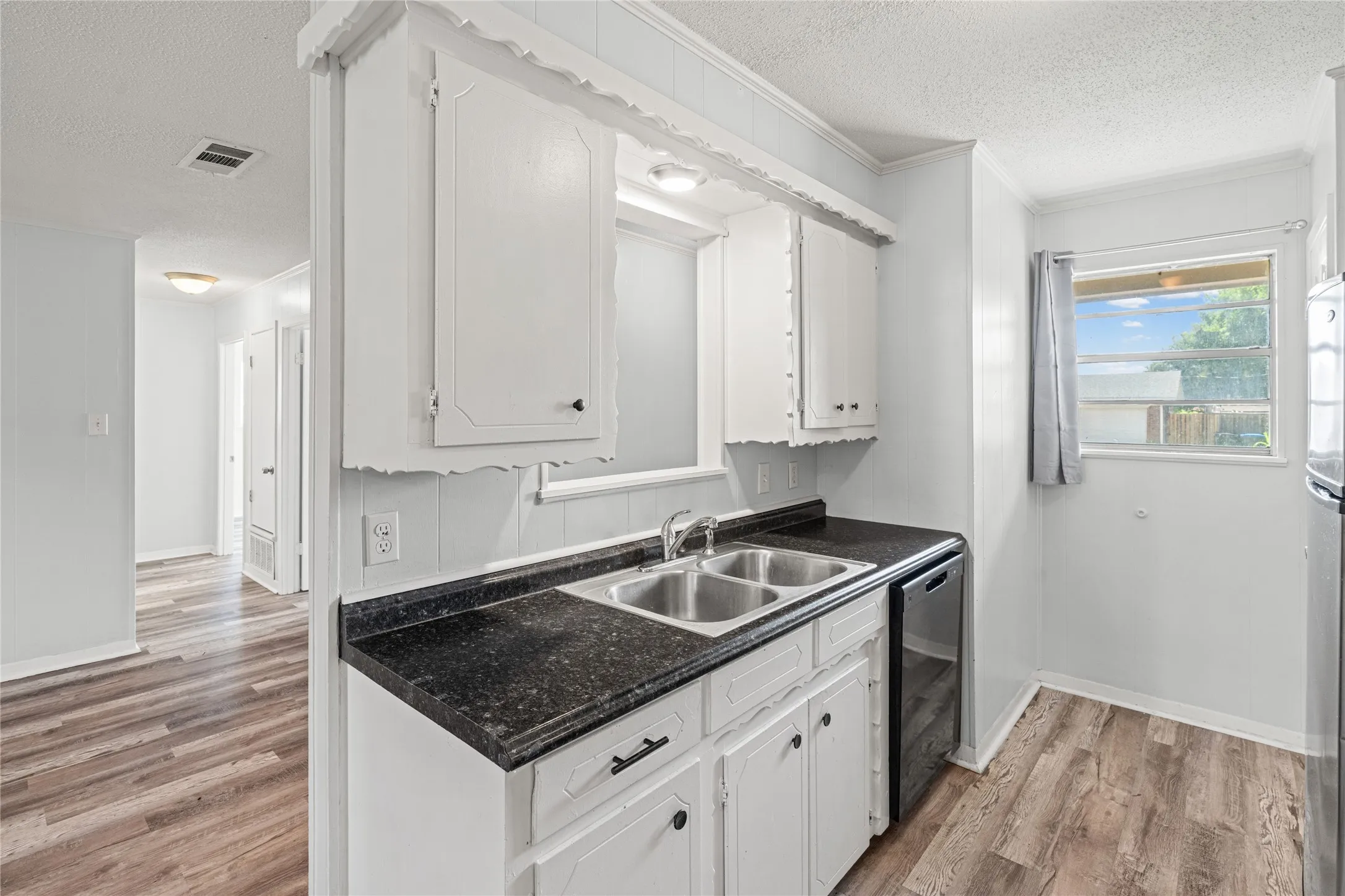 Kitchen featuring white cabinetry, dark countertops, a double-basin stainless steel sink, and wood-finish flooring
