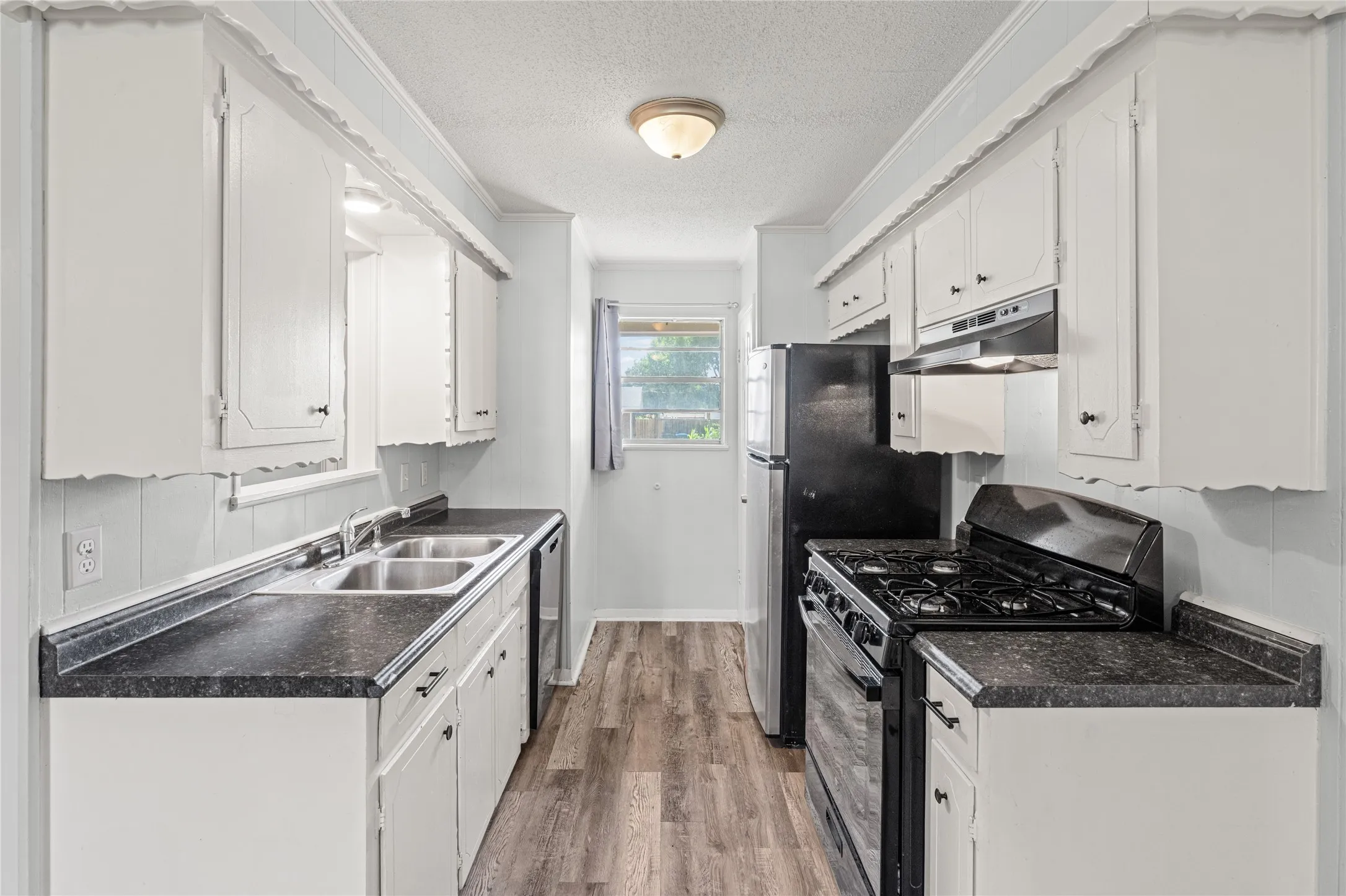 Galley kitchen featuring white cabinetry, dark countertops, wood-finish flooring, and a window for natural light