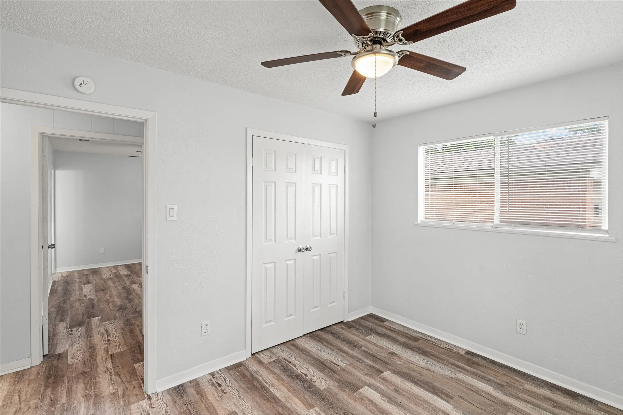 Room featuring wood-finish flooring, a ceiling fan with integrated lighting, a double-door closet, and a window with horizontal blinds