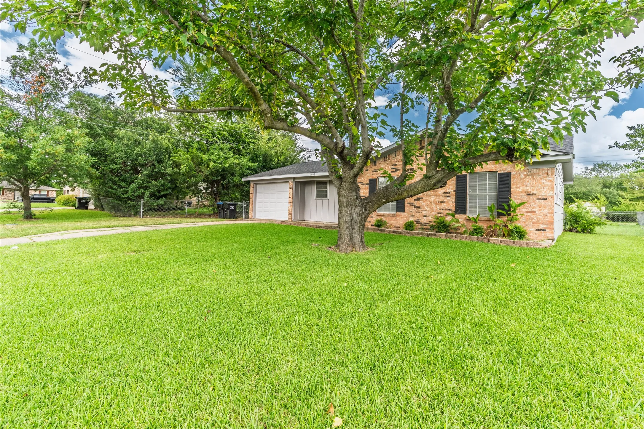 Expansive front yard with a mature shade tree, a brick exterior, and a single-car garage