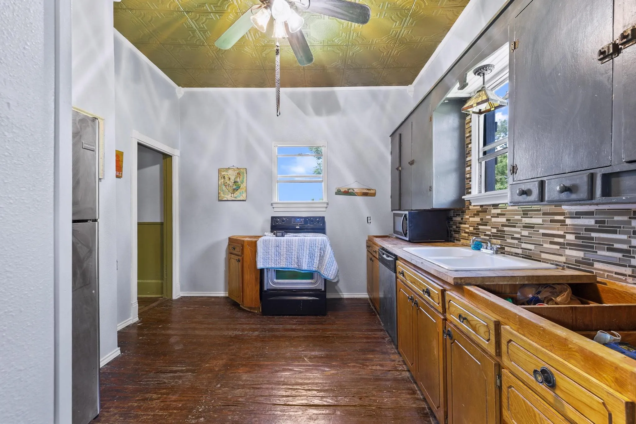 Kitchen featuring a pressed tin ceiling, wood-finish flooring, a tile backsplash, and wood cabinetry