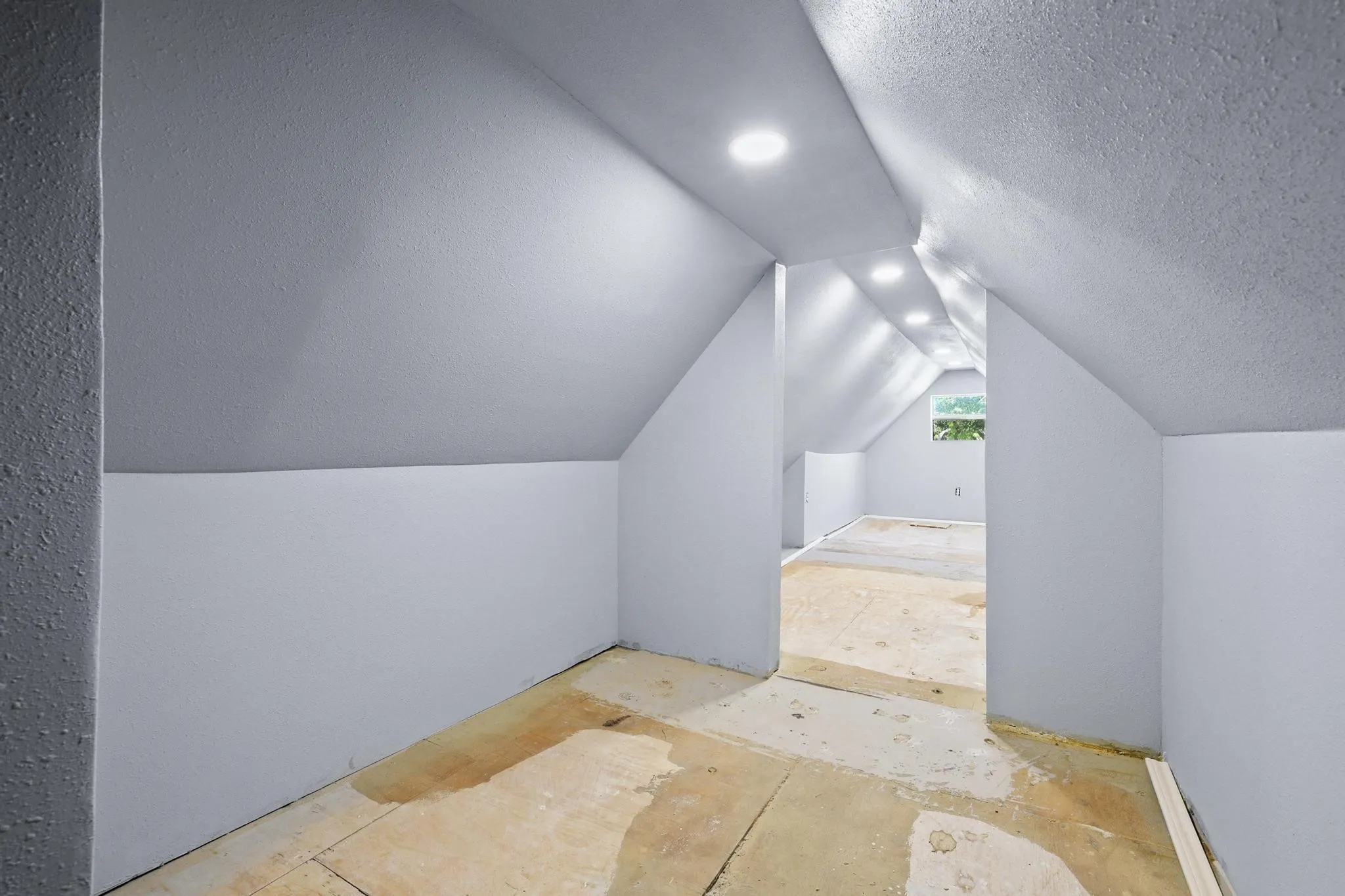 Attic space featuring sloped ceilings, recessed lighting, a window, and light gray painted walls