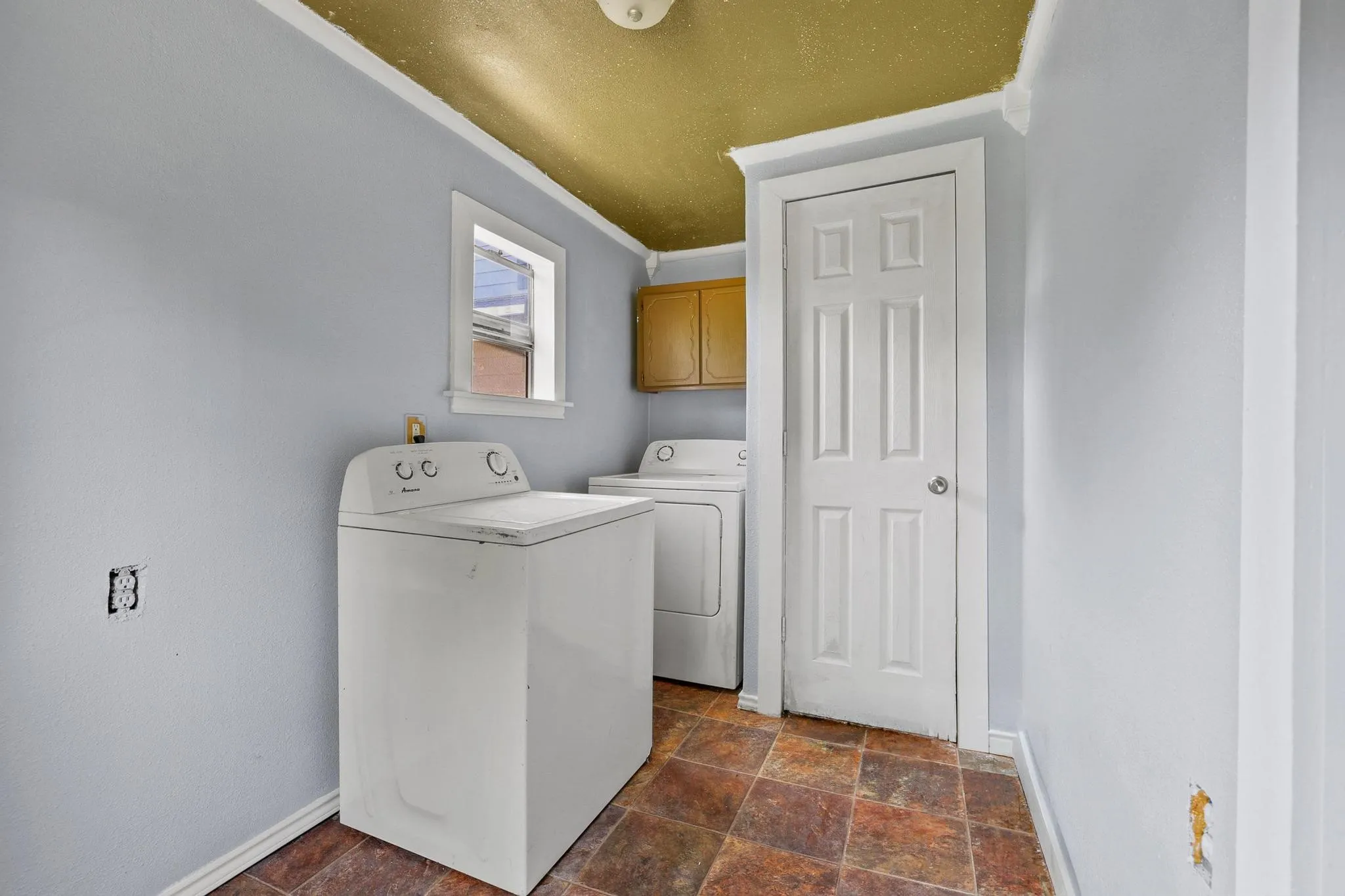 Utility space featuring a window, brown tile-look flooring, light blue walls, and a built-in wood-tone cabinet