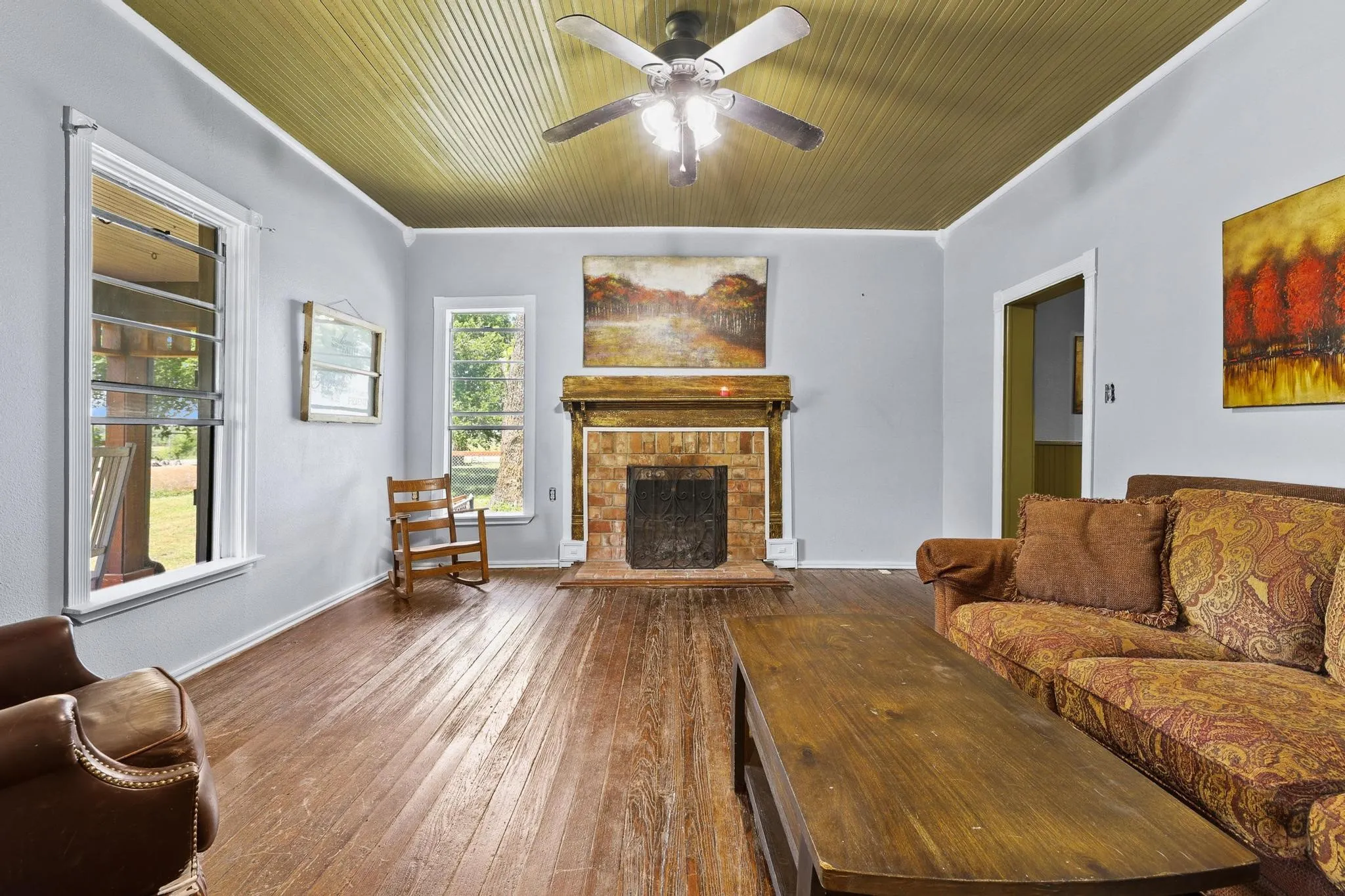 Spacious living area featuring wood-finish flooring, a brick fireplace with a wood mantel, and multiple windows