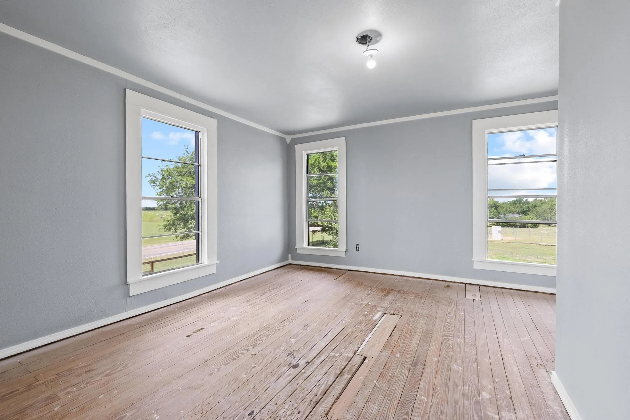 Upstairs bedroom featuring windows with white trim, light gray walls, white baseboards, and white crown molding