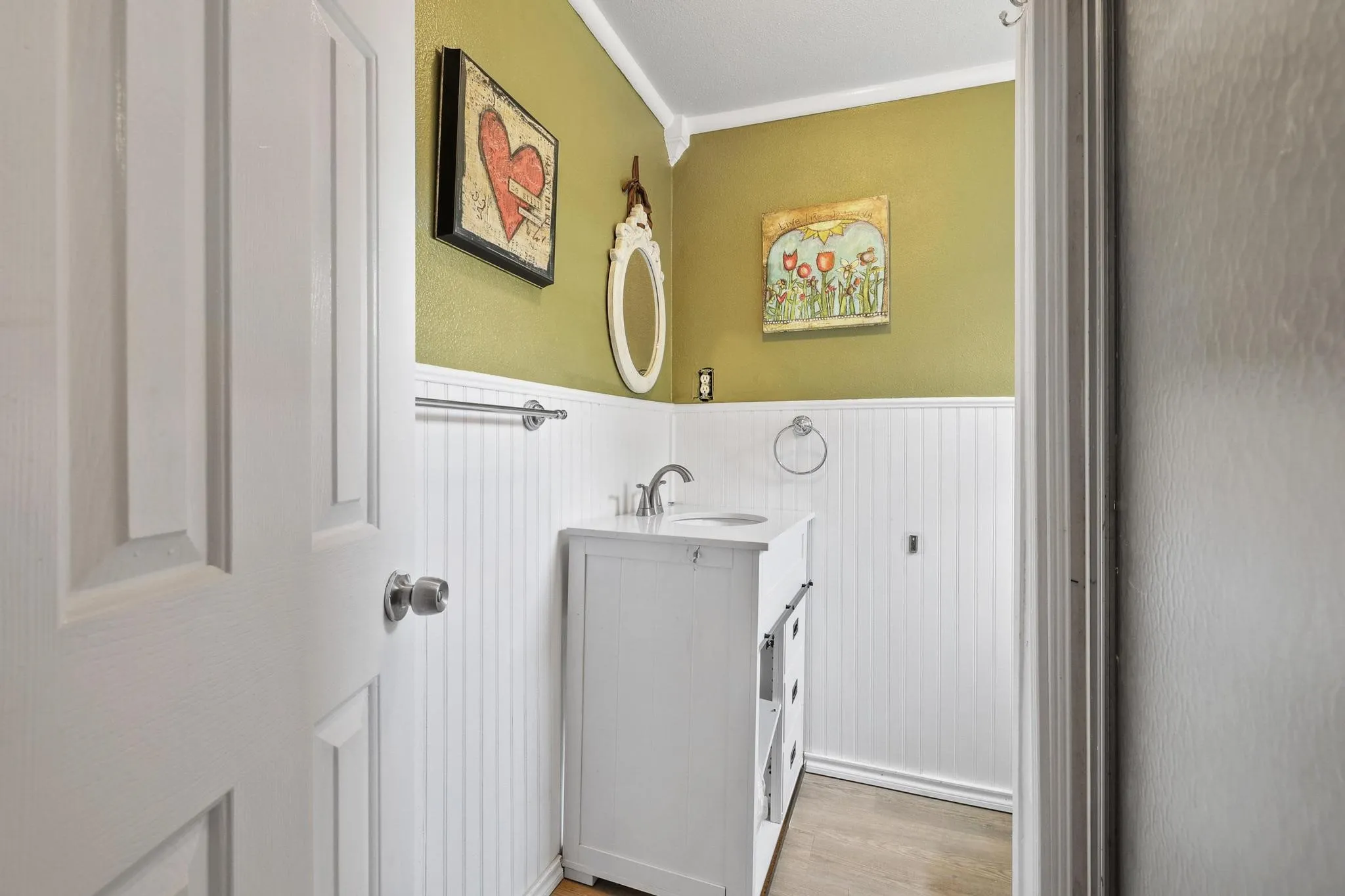 Powder room featuring a white single-sink vanity, beadboard wainscoting, a chrome faucet, and wood-finish flooring