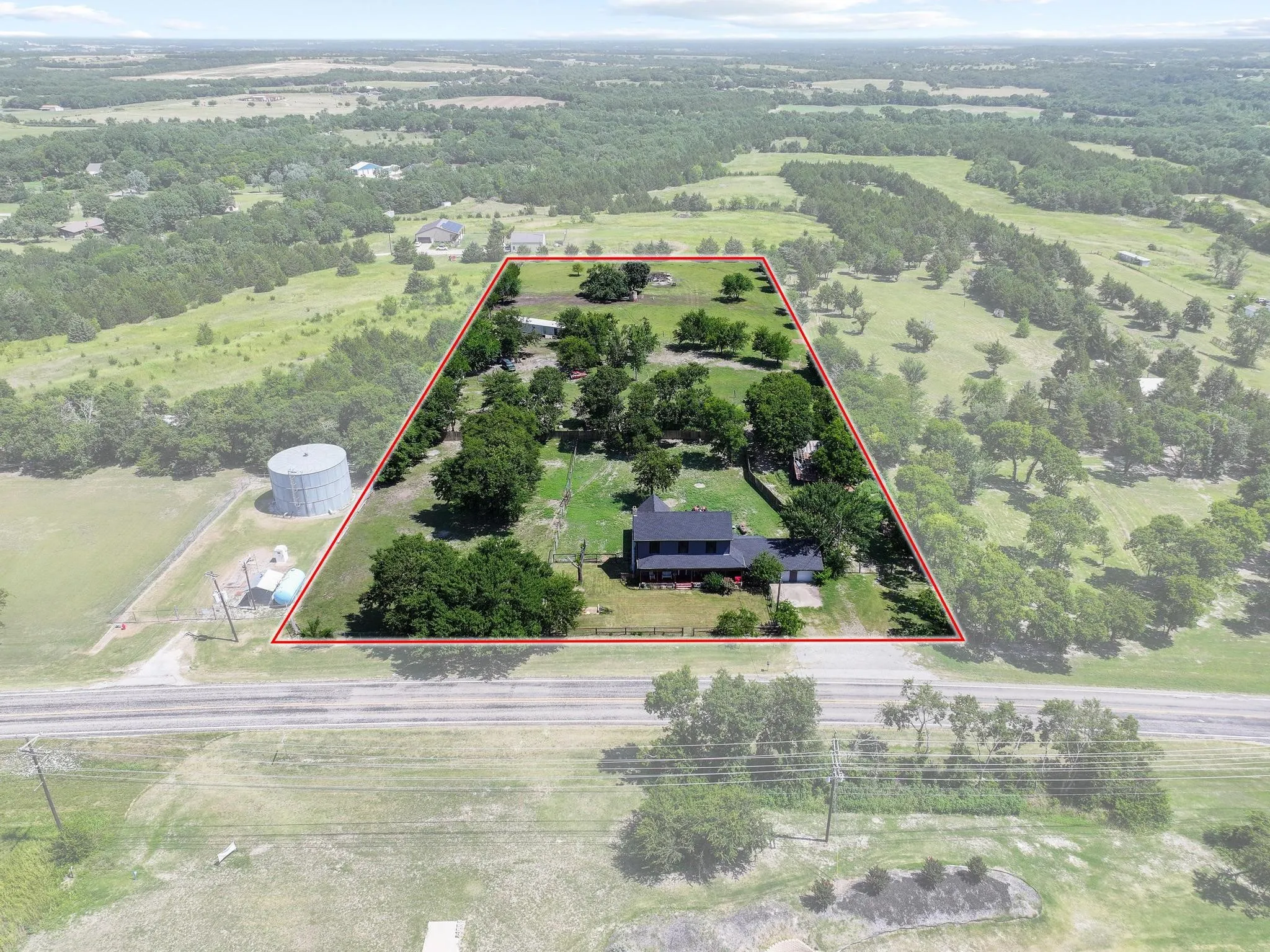Expansive property featuring a black-roofed residence, mature trees, and a defined boundary line