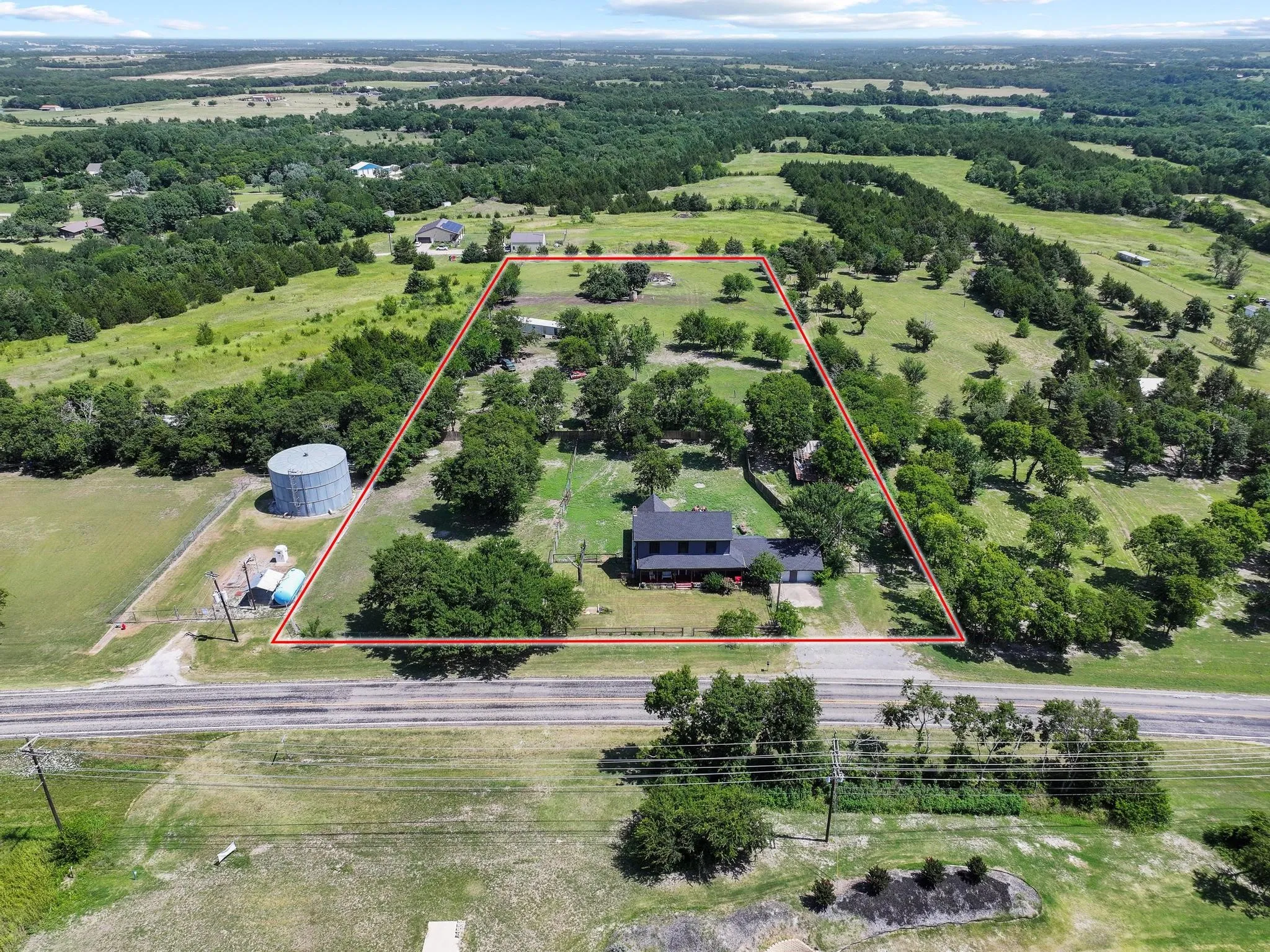 Expansive rural property featuring a large structure with a dark roof, surrounded by mature trees and verdant fields