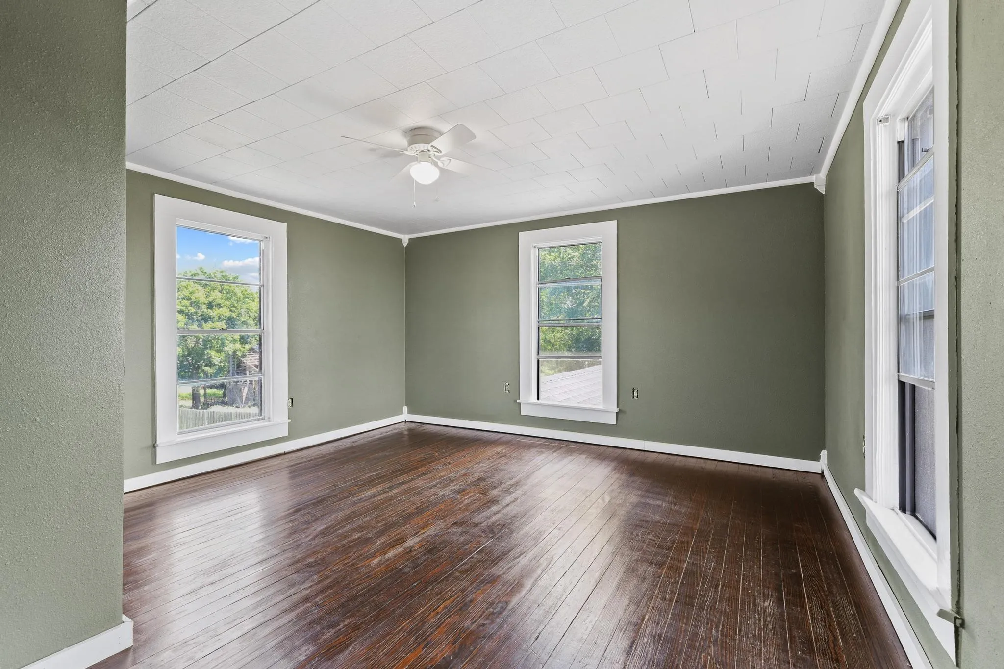 Upstairs bedroom featuring rich wood-finish flooring, a white ceiling fan, and large windows