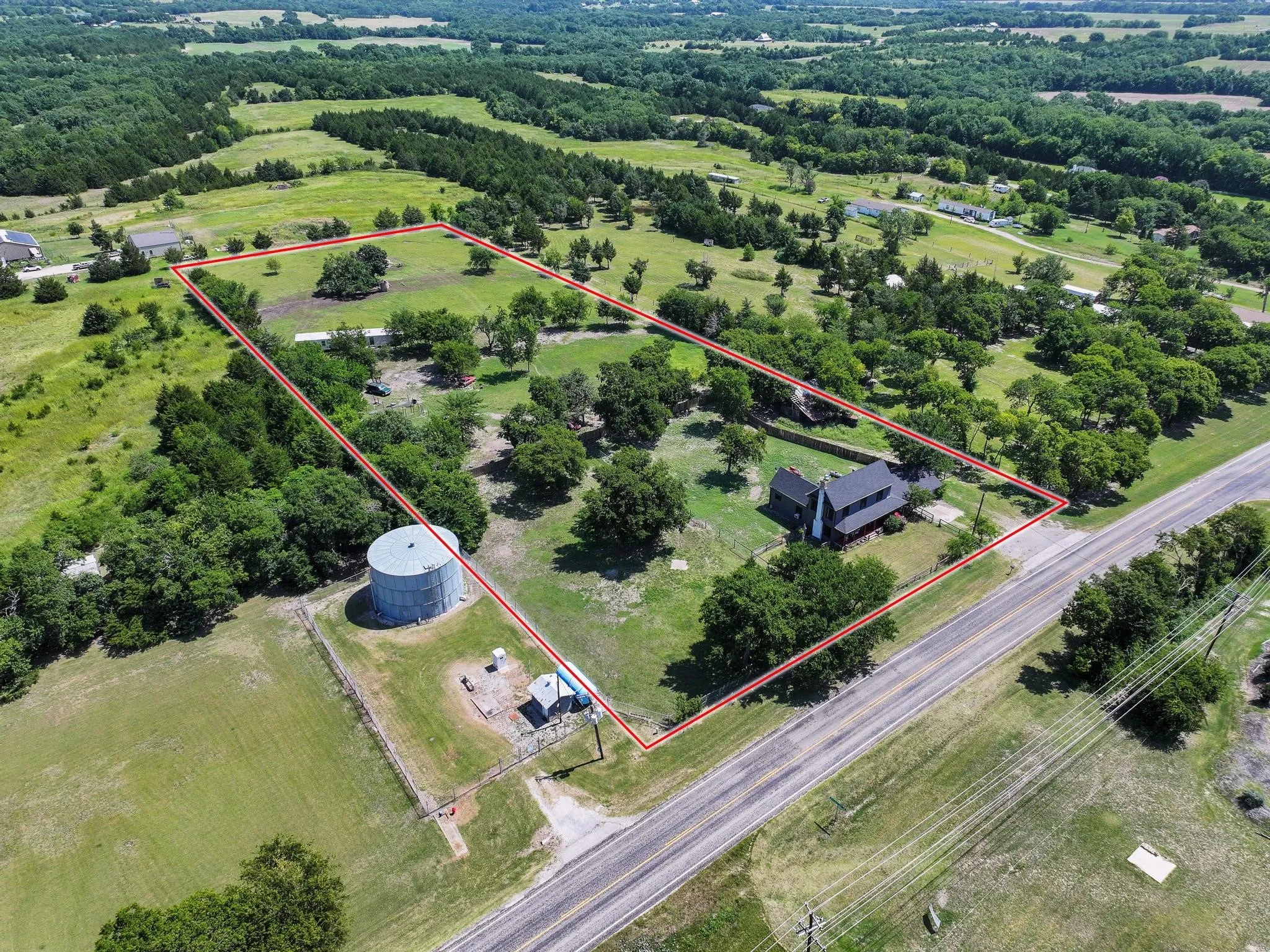 Expansive rural property featuring a main residence, mature trees, open green spaces, a water tower, and a paved road frontage