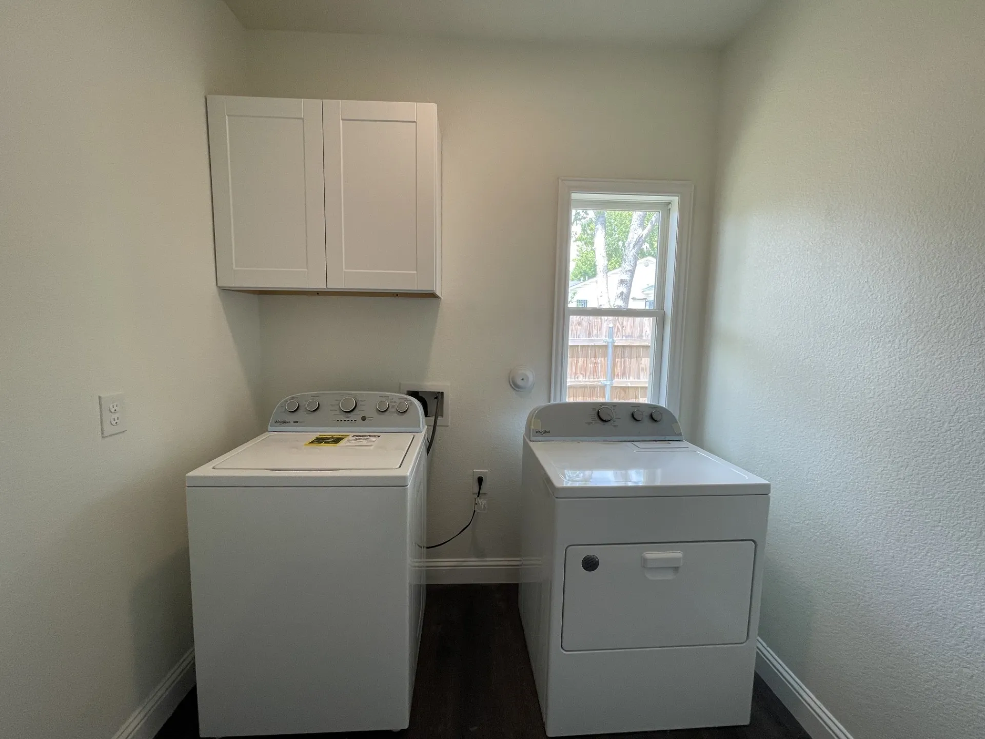 Dedicated laundry area featuring dark wood-finish flooring, white baseboards, and a single-pane window with white trim