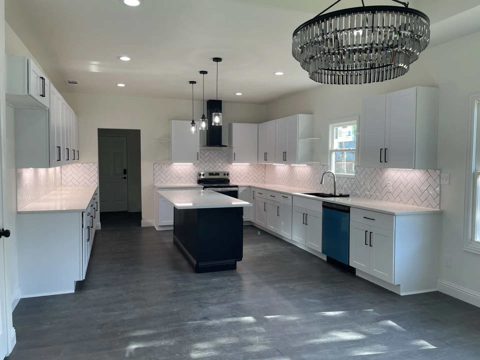 Modern kitchen featuring a central island with contrasting base cabinetry, ample white perimeter cabinetry, light-toned countertops, and a white herringbone tile backsplash
