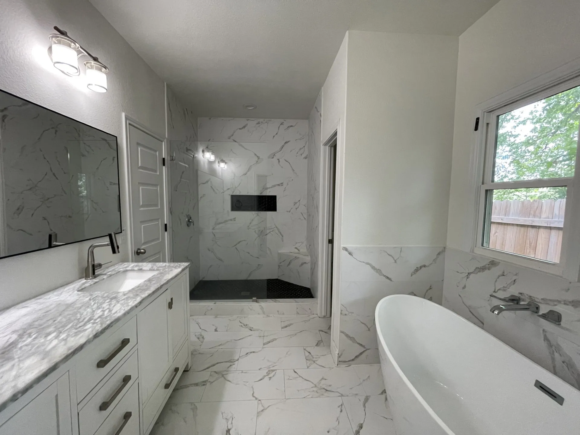 Modern bathroom featuring a freestanding soaking tub, a spacious walk-in shower with a built-in niche, and a double vanity with a stone countertop