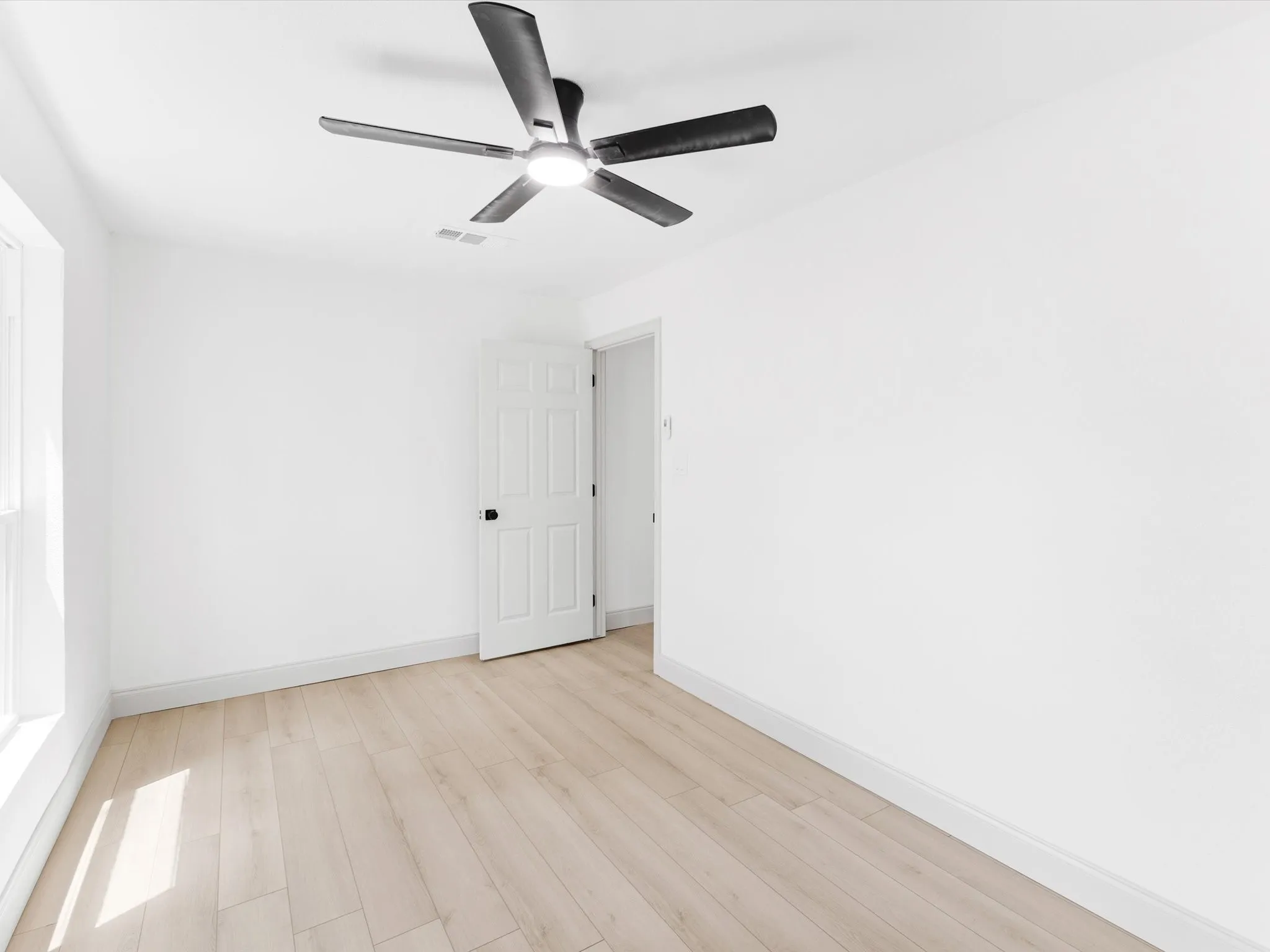 Room featuring wood-finish flooring, a contemporary ceiling fan with integrated lighting, white baseboards, and a white panel door with black hardware