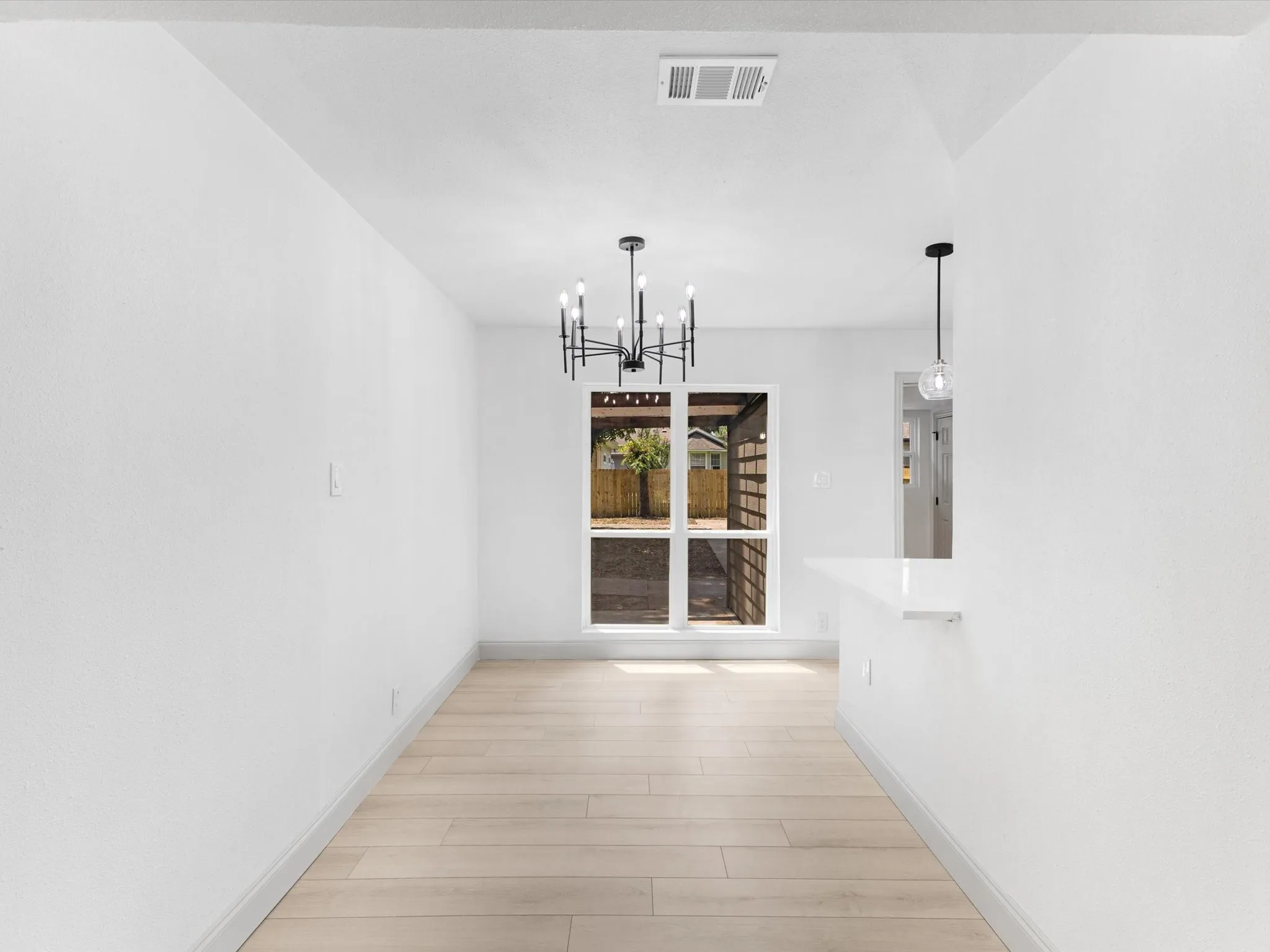 Open-concept dining area featuring wood-finish flooring, a modern black chandelier, and a breakfast bar with a white countertop