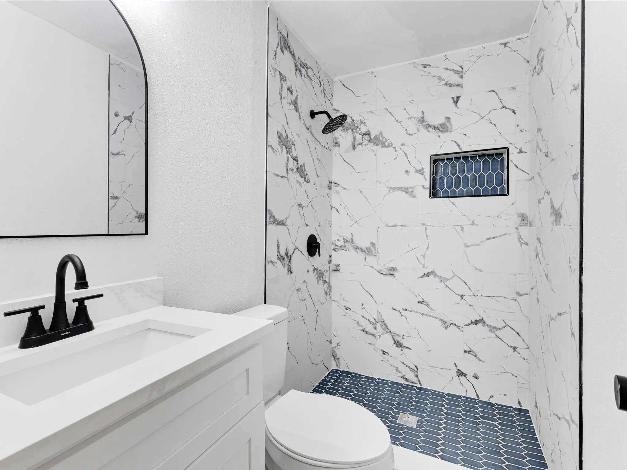 Modern bathroom featuring a walk-in shower with large format marble-look tile walls and blue hexagonal floor tile
