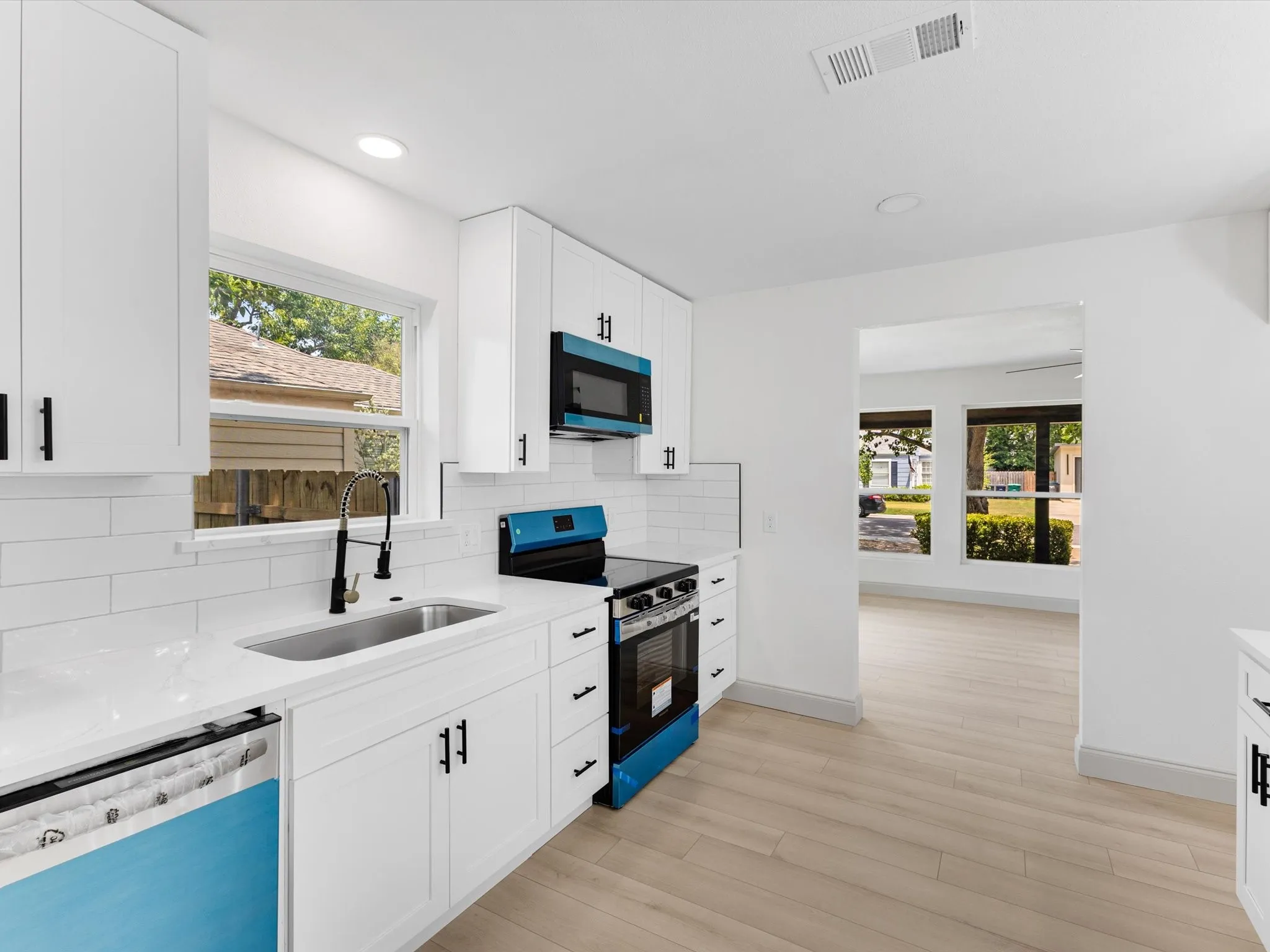 Contemporary kitchen featuring white shaker cabinetry, white subway tile backsplash, white countertops, stainless steel sink with a matte black pull-down faucet, and wood-finish flooring